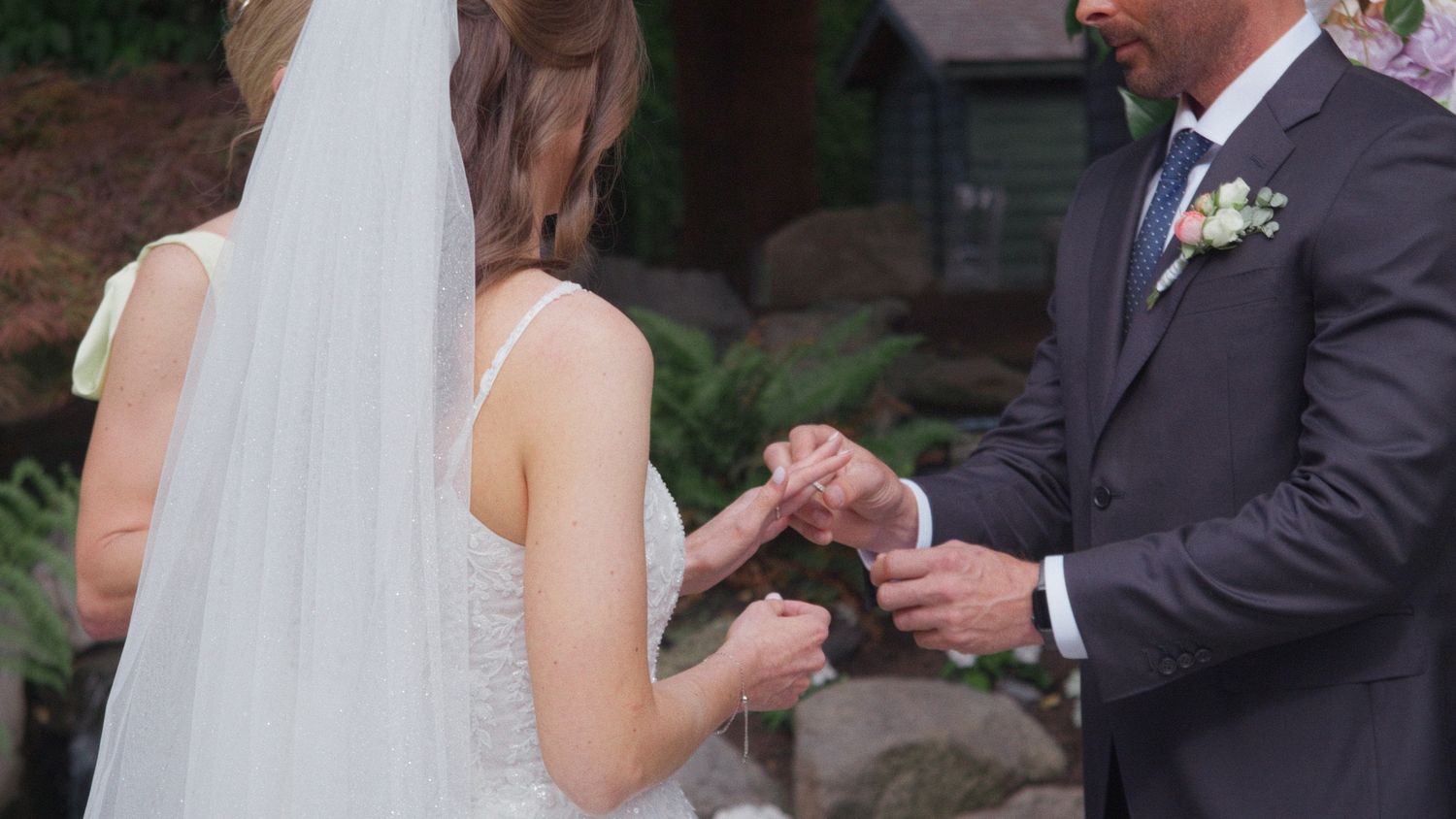 Bride and groom exchanging rings during an outdoor wedding ceremony surrounded by lush greenery.