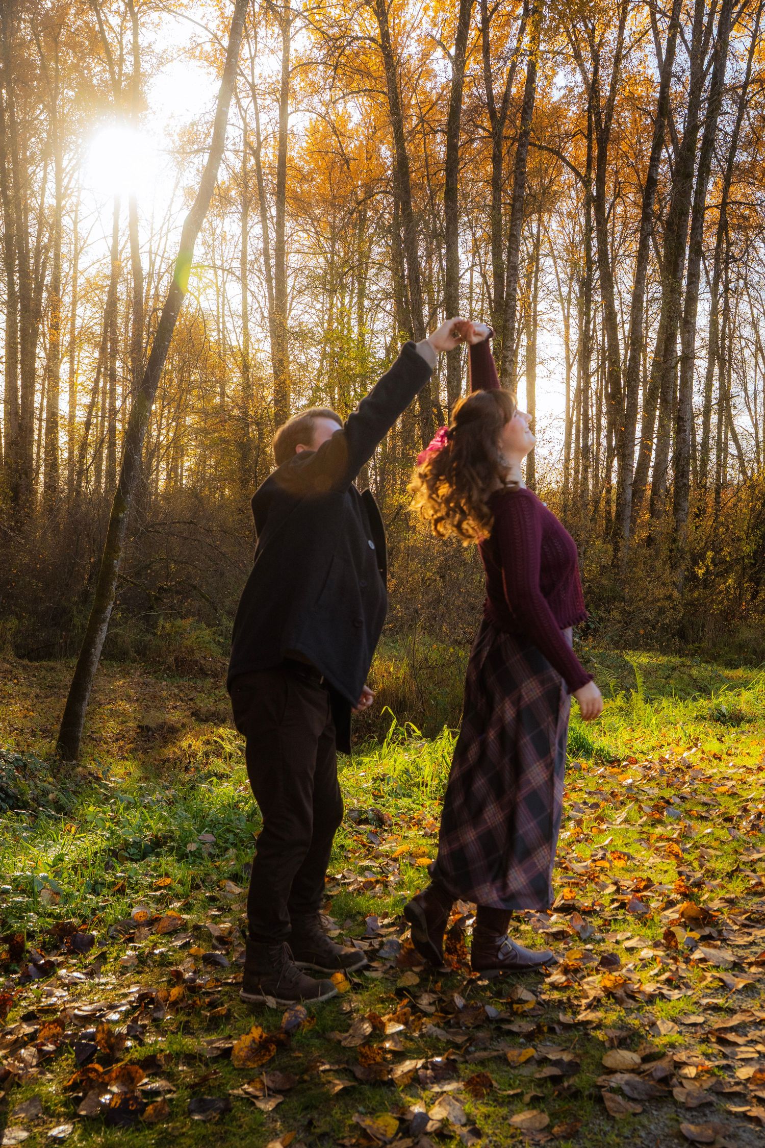 Couple dancing playfully in a golden autumn forest with sunlight streaming through colorful fall foliage.