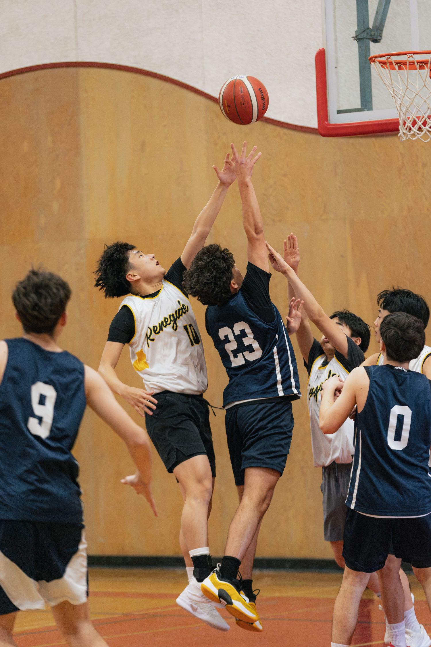Player #23 in navy uniform battles for a rebound against Renegades players near the basket in youth basketball game.