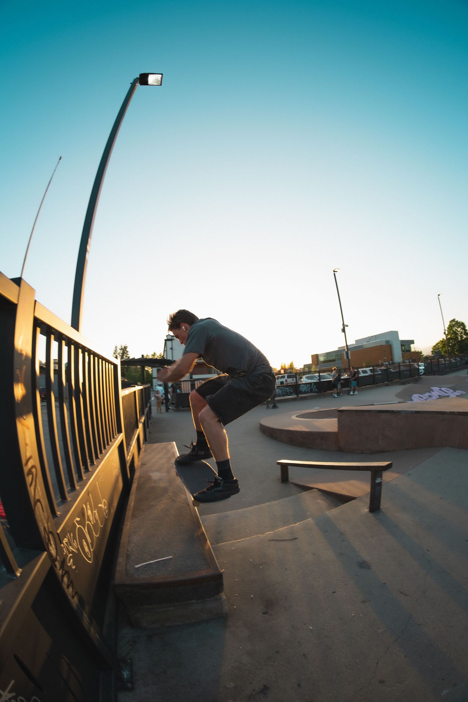 Skateboarder performing a trick on a ledge at an outdoor skate park during golden hour.