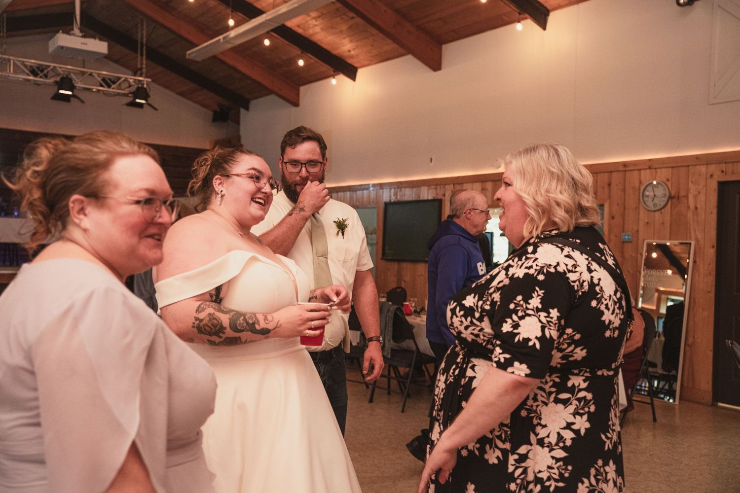Bride in white gown socializes with guests including a tattooed bridesmaid at the wedding reception.