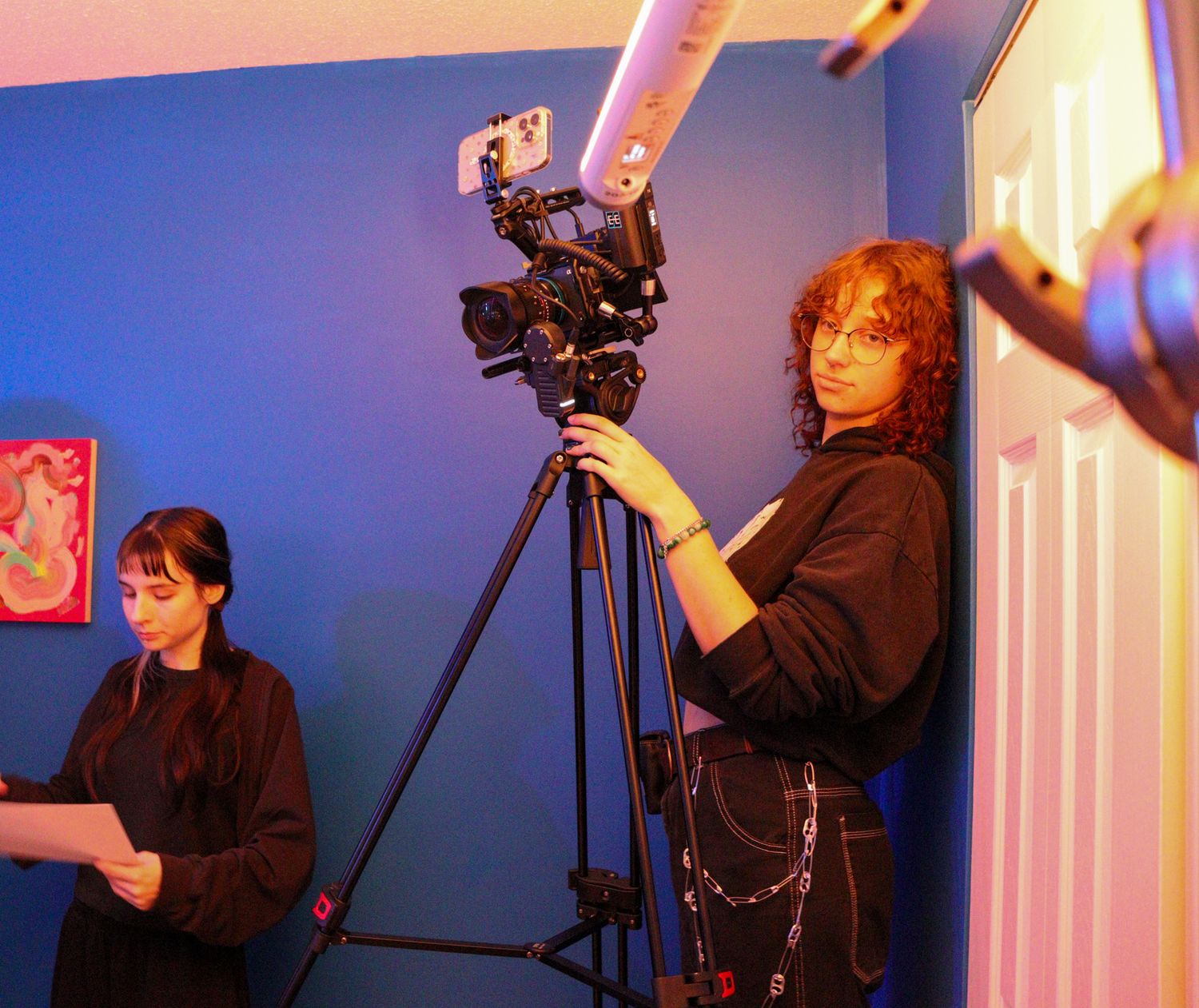 Cinematographer operating a camera on a tripod in a blue-walled room during a film shoot.