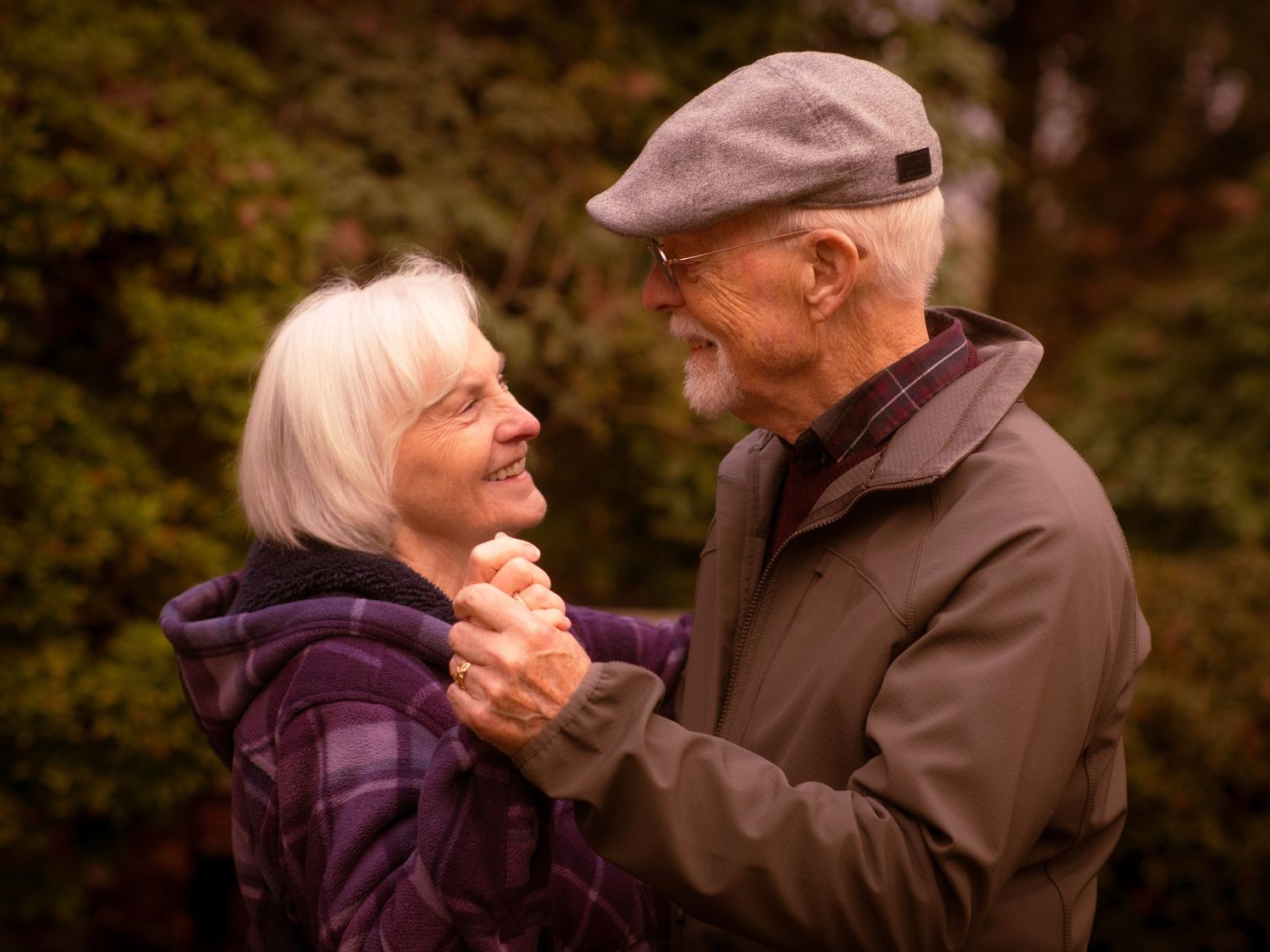 Senior couple holding hands and smiling at each other in a lush green garden.