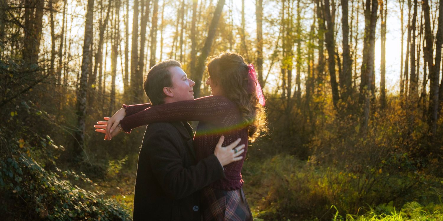 Couple embracing warmly in a sunlit autumn forest with golden light streaming through the trees.