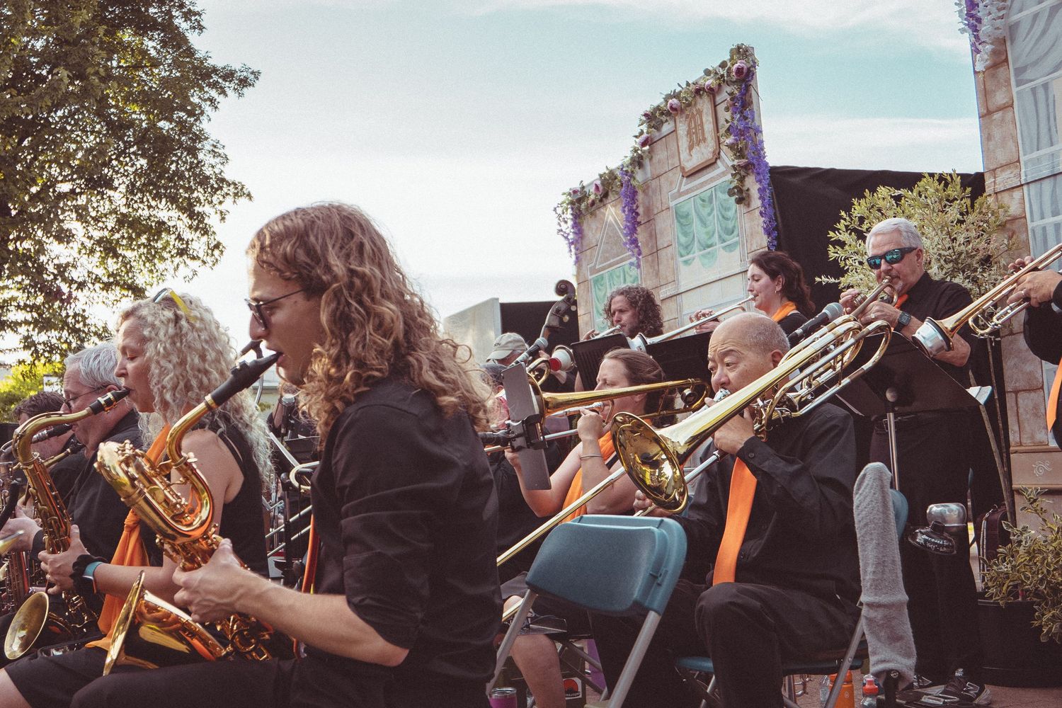 Outdoor brass band performance with musicians playing trombones and horns in black attire at a sunny festival.