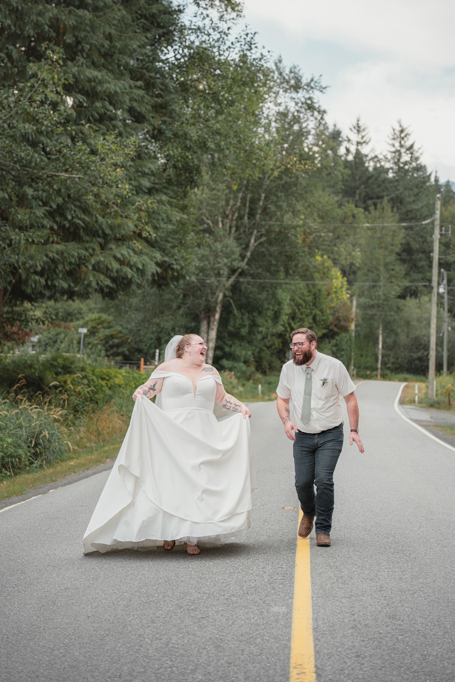 Bride and groom walking down a rural road surrounded by lush green trees on their wedding day.