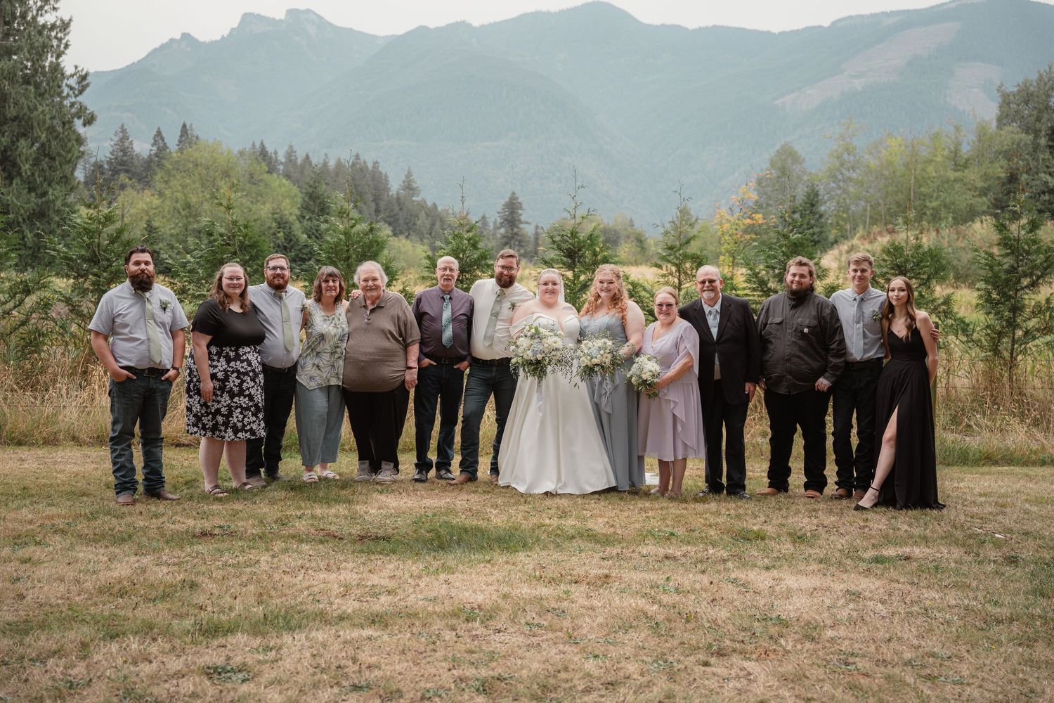 Large wedding family group portrait outdoors with mountain and forest backdrop on wedding day.