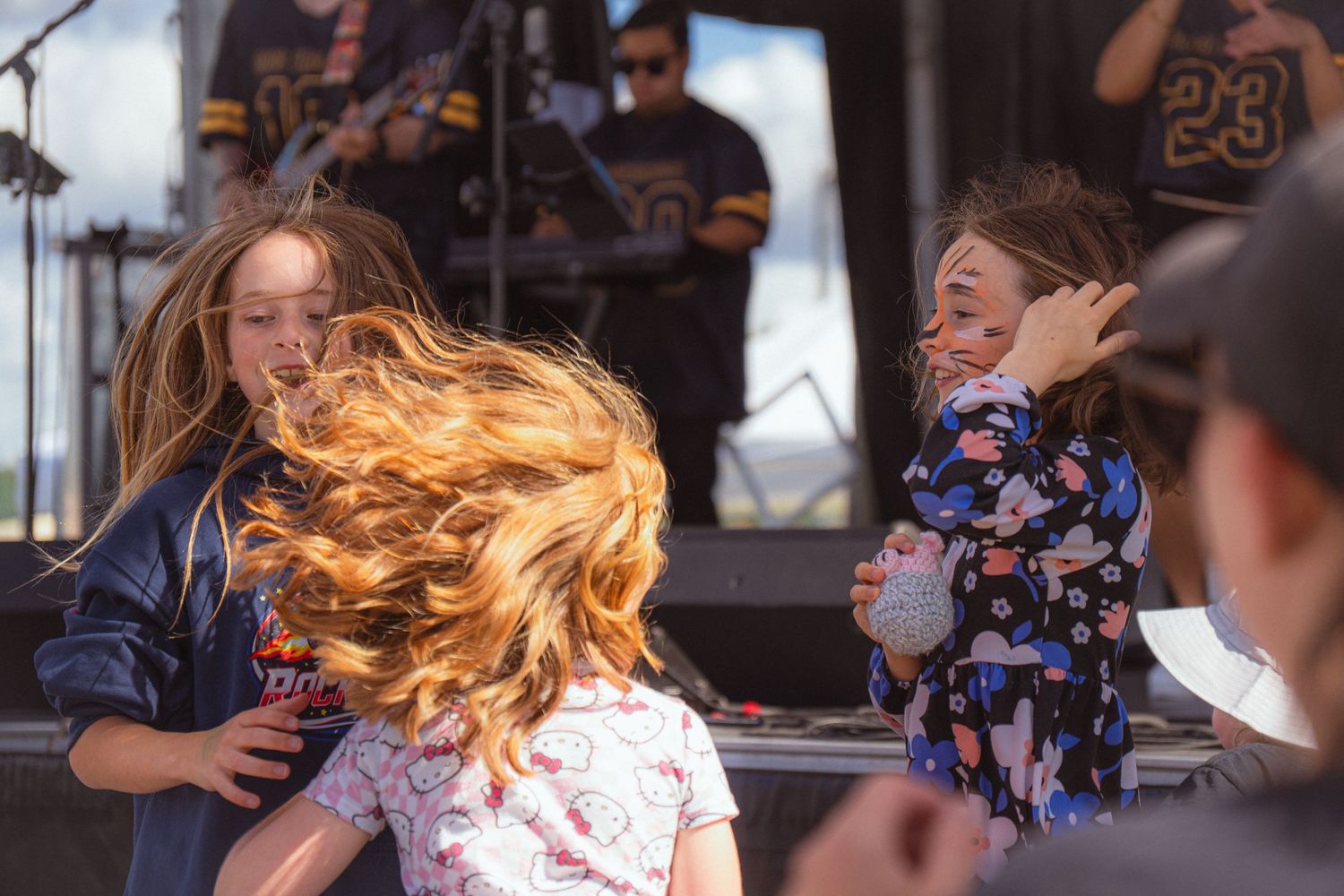 Children dancing energetically at outdoor music festival with hair flying in motion.