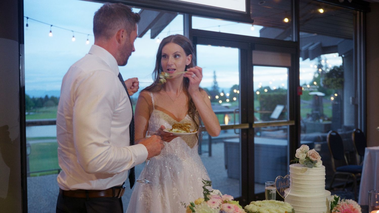 Bride and groom sharing wedding cake at elegant evening reception venue.