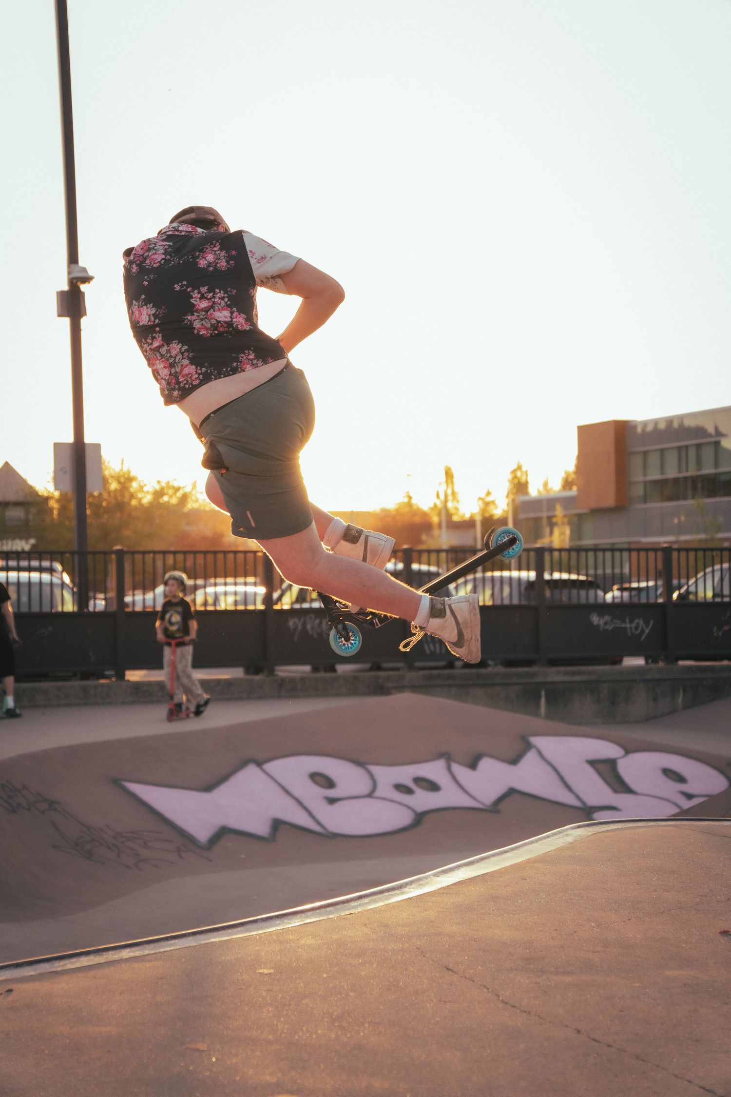 Skateboarder in floral vest performing an aerial trick over a graffiti ramp at golden hour.