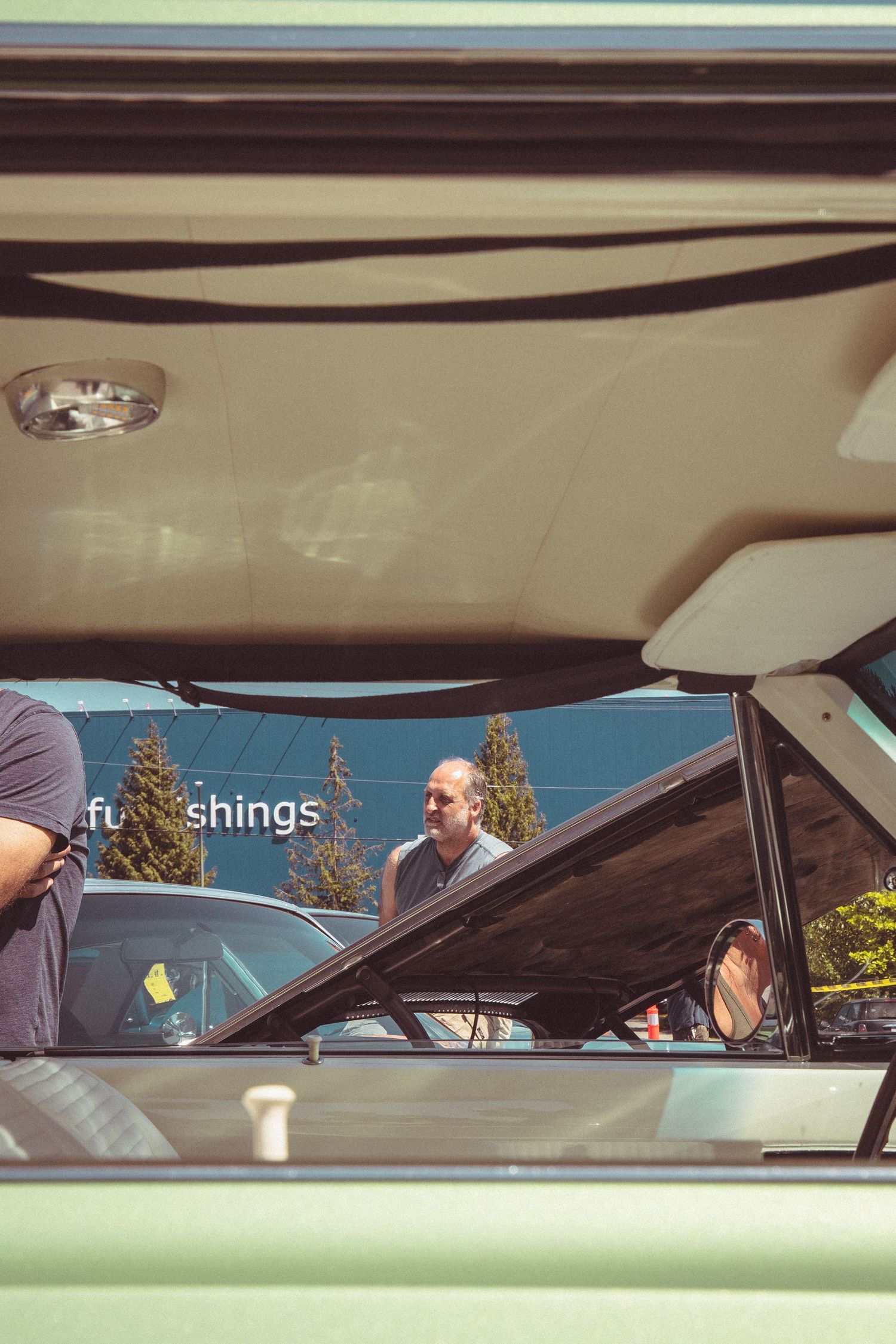 View through a classic car window at a vintage auto show with people browsing in a sunny parking lot.