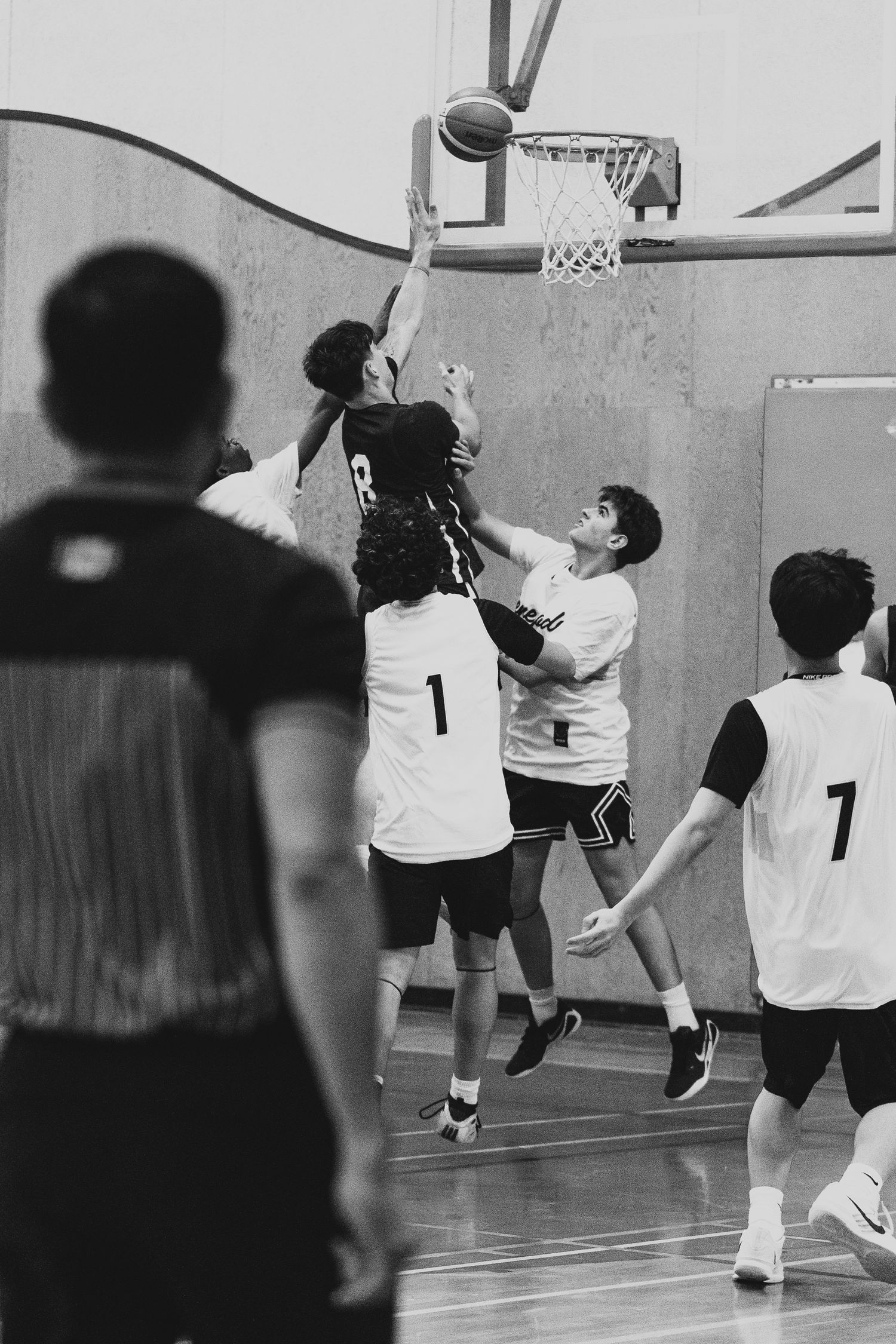 Basketball player dunks over defenders during indoor game as teammates in jerseys 1 and 7 watch.