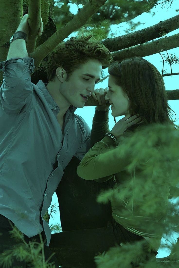 A young couple shares a romantic moment among tree branches, their faces close together in a moody green-tinted forest setting.
