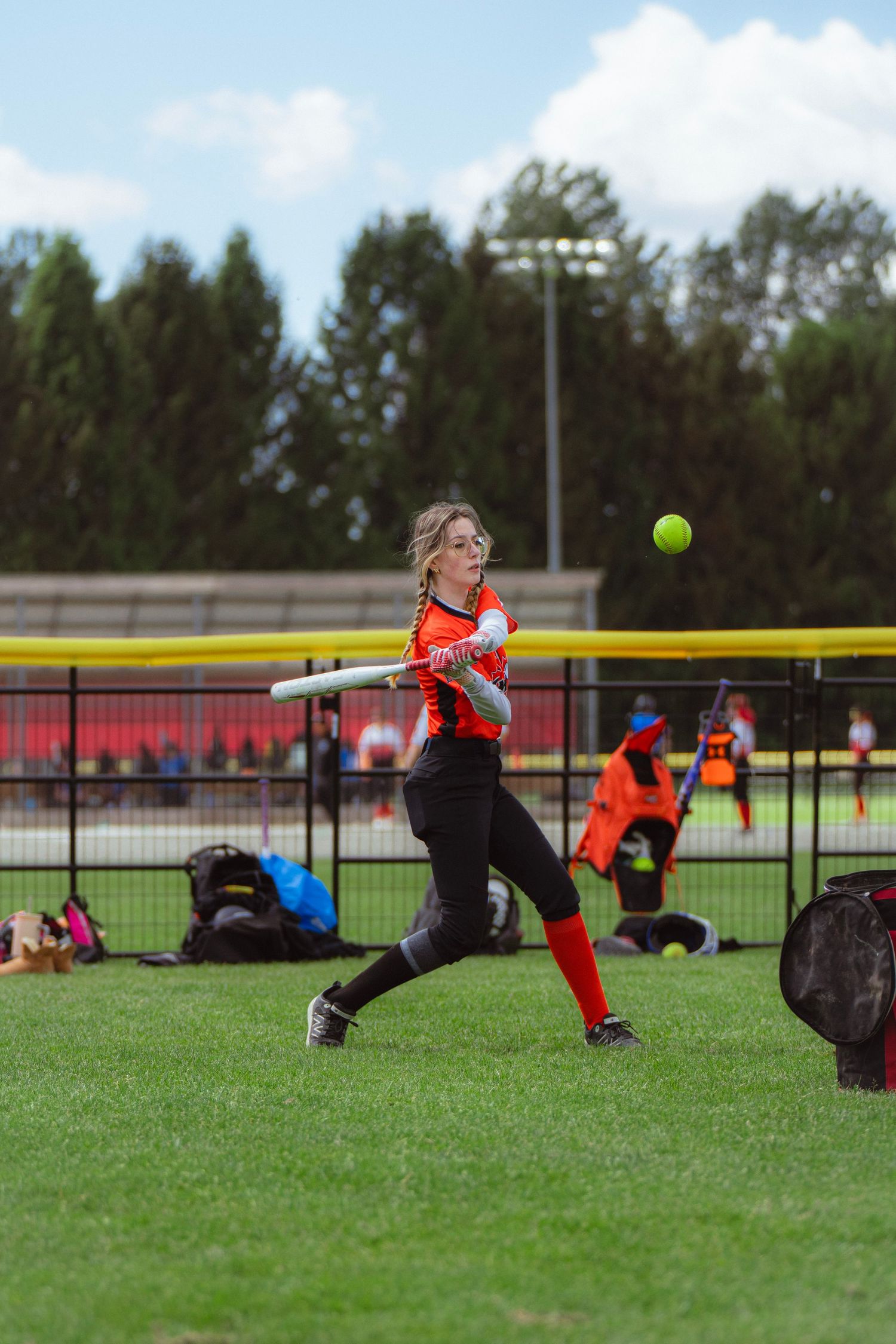Young female softball player in orange and black uniform hitting ball during practice session.