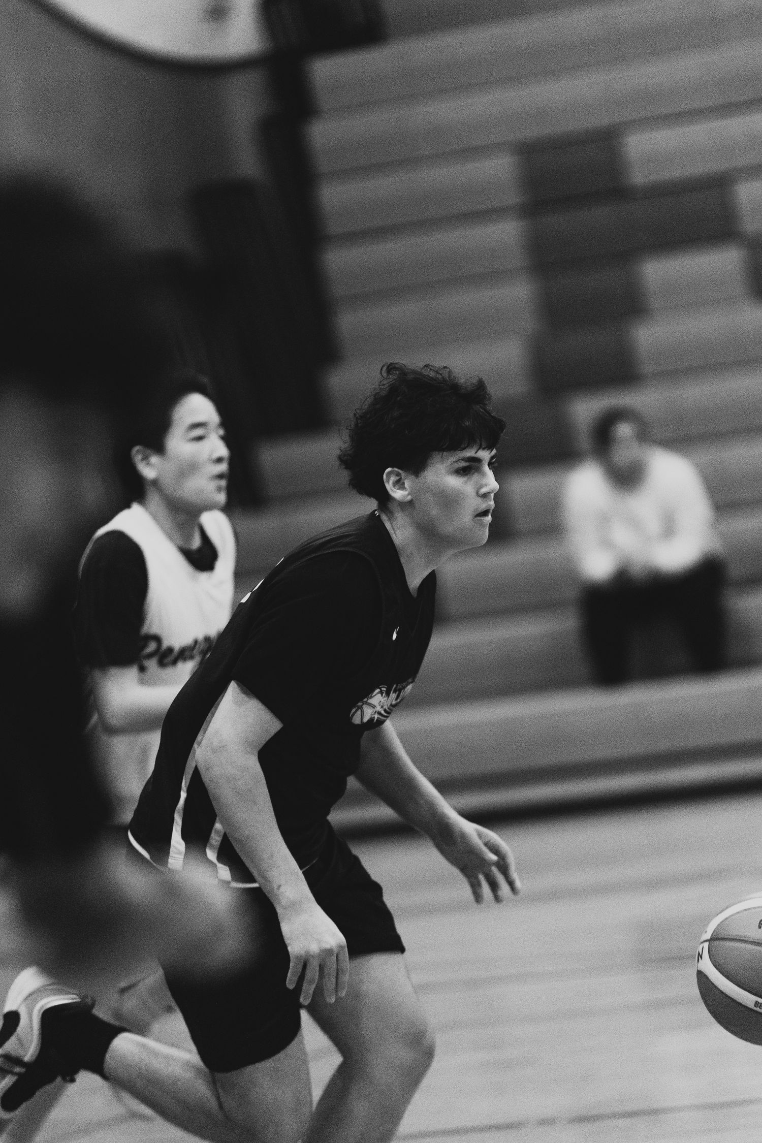 Young basketball player with curly hair dribbles the ball during an indoor gymnasium game.