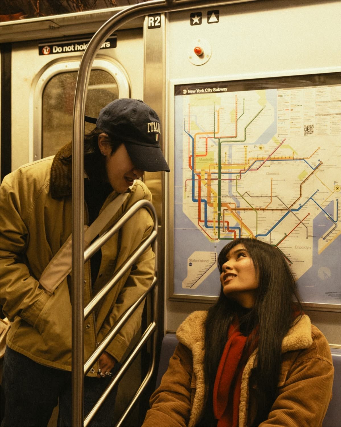 Two people share a moment on a New York City subway car, with an MTA route map visible on the wall behind them.