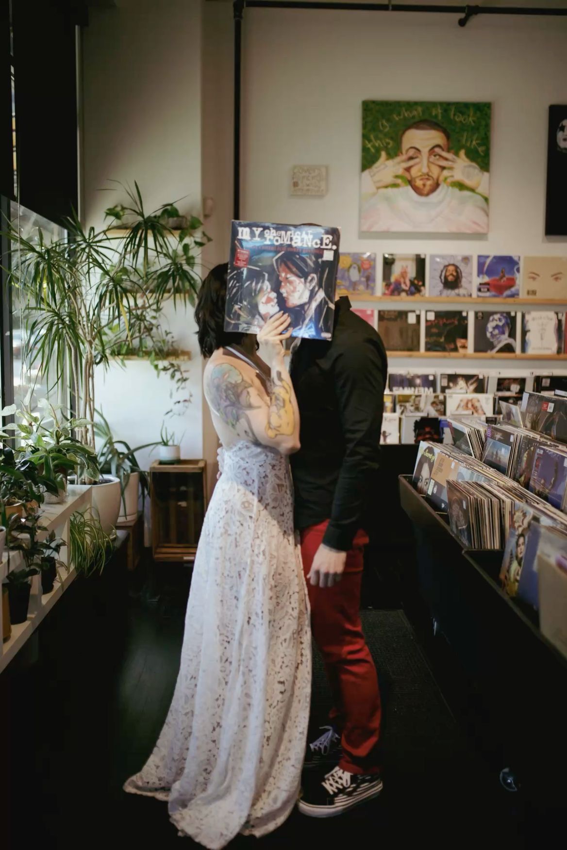 Couple kissing behind a vinyl record album in a music store, bride in lace dress and groom in black jacket.