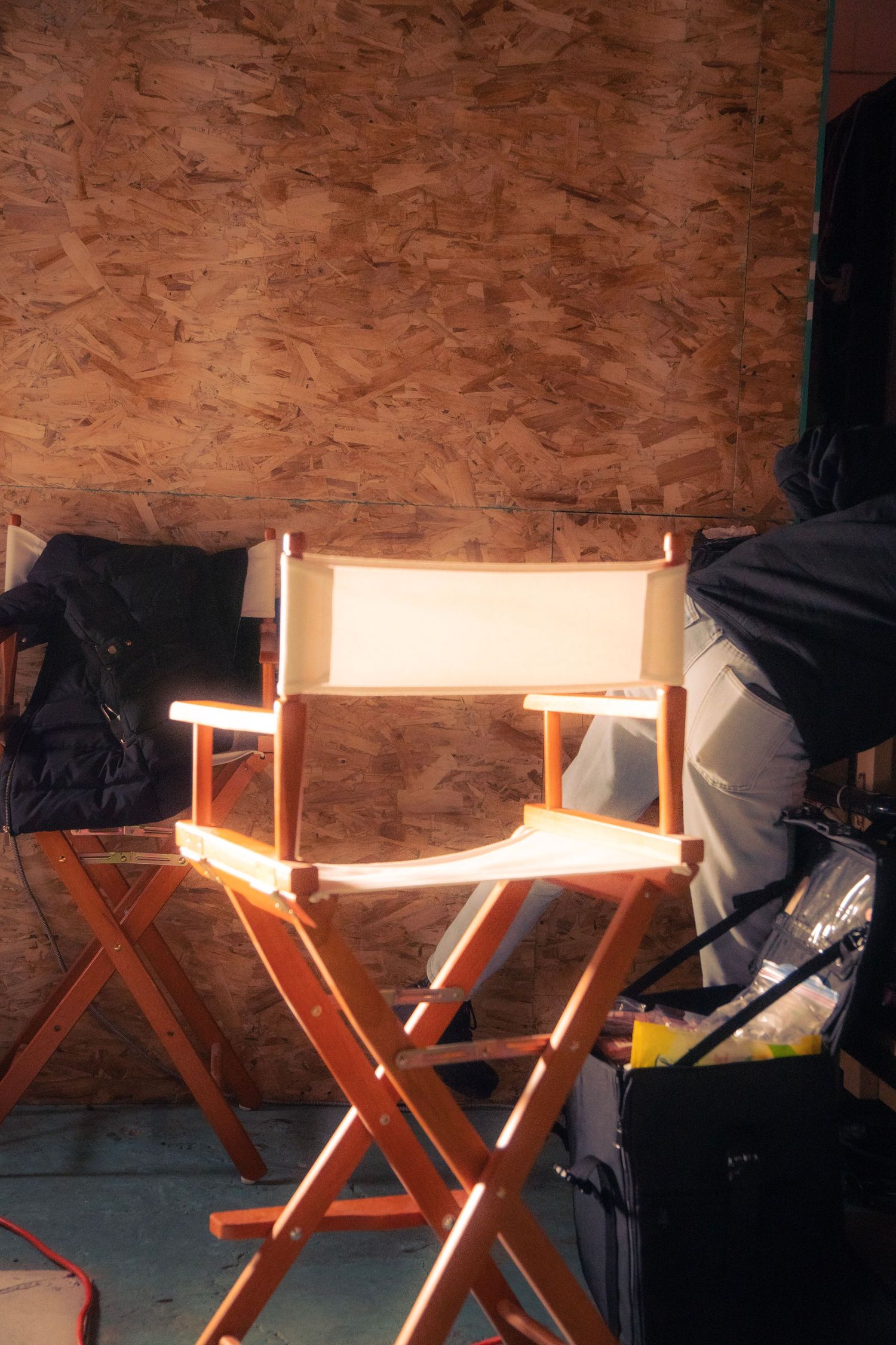 Empty director's chair illuminated by warm light against a plywood wall on a film set.