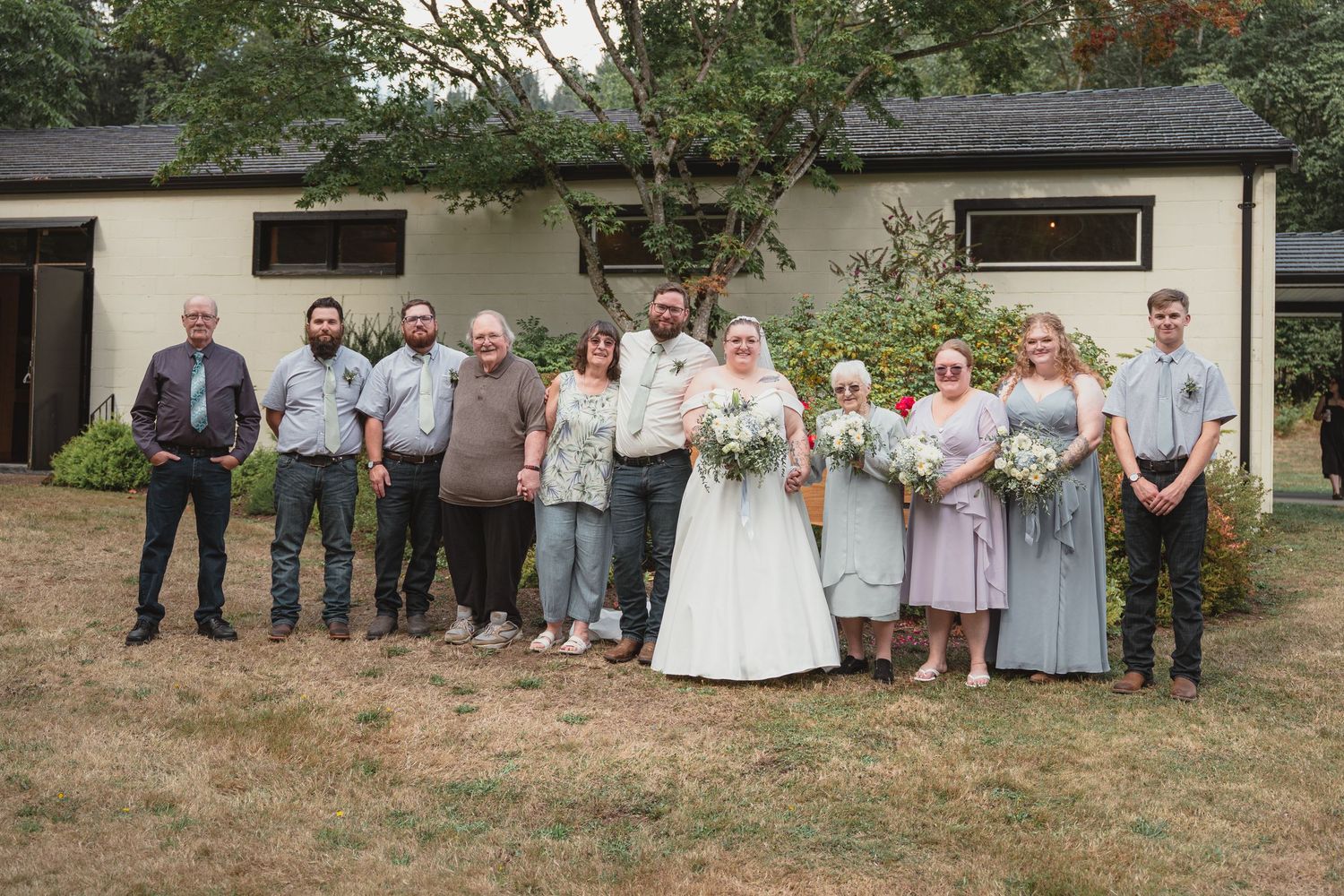 Wedding party poses outdoors in front of white building, bride in white gown with bridesmaids in blue dresses.