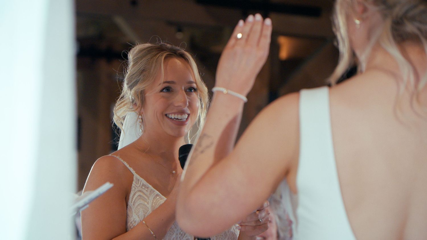 Smiling bride in lace dress shares joyful moment with reflection in mirror before wedding.
