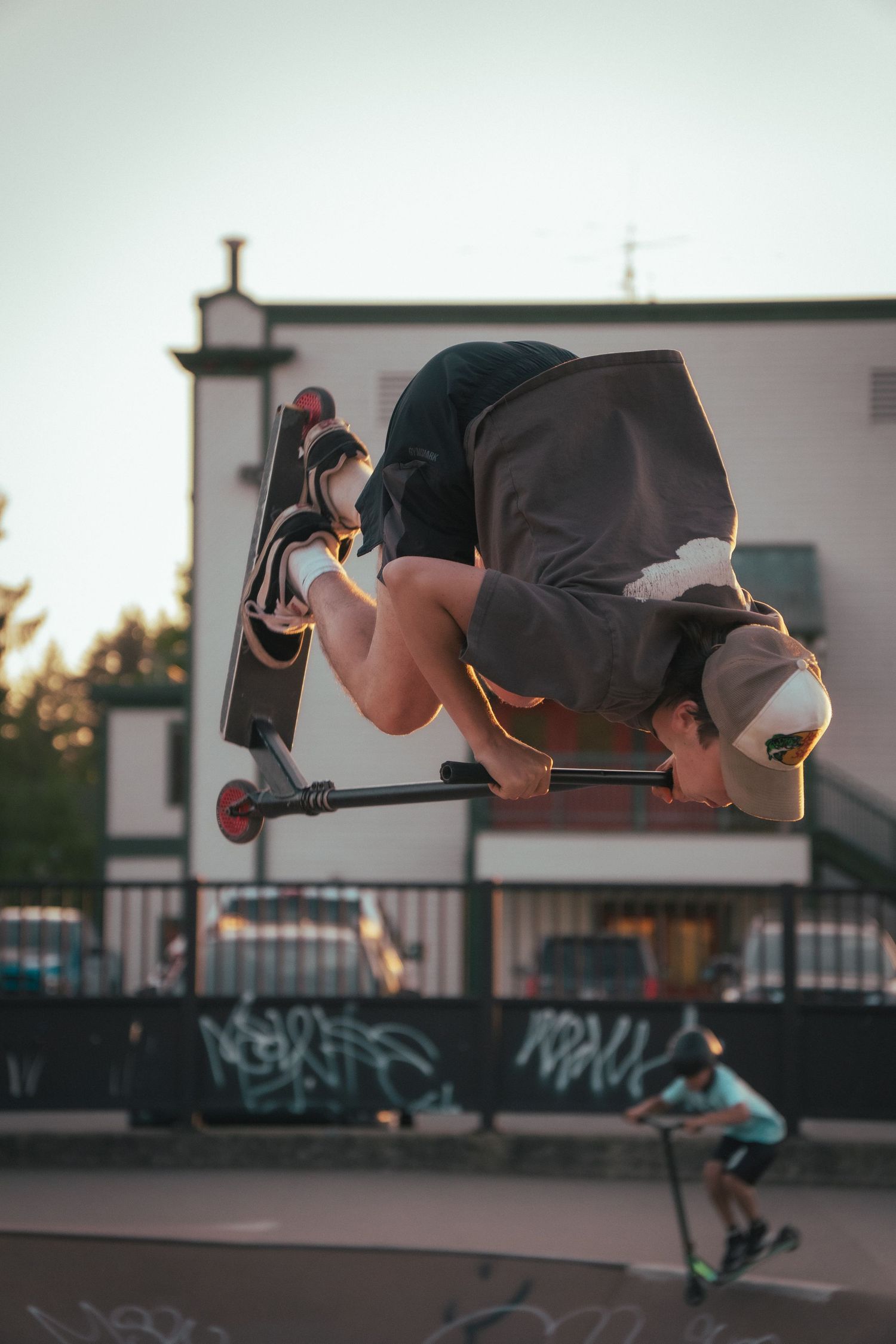 Scooter rider performing an inverted aerial trick at a skate park during sunset.