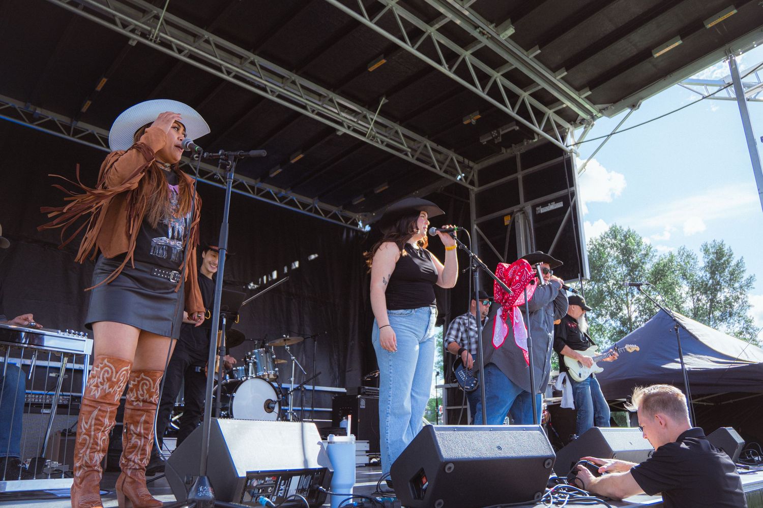 Two female country singers performing together on outdoor festival stage in cowboy hats.