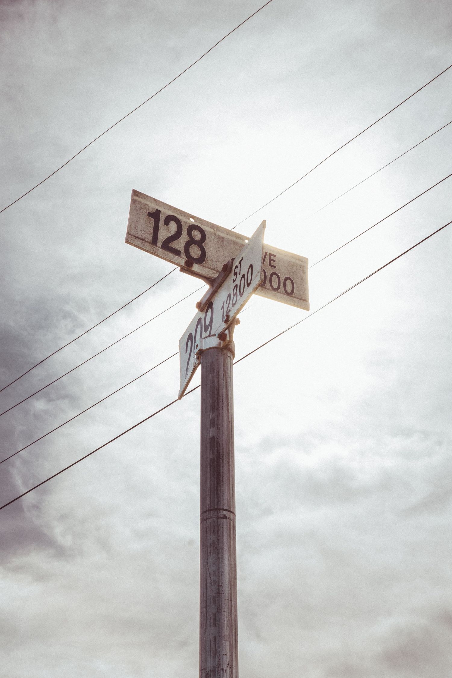 Weathered street sign post showing number 128 with power lines against overcast sky.