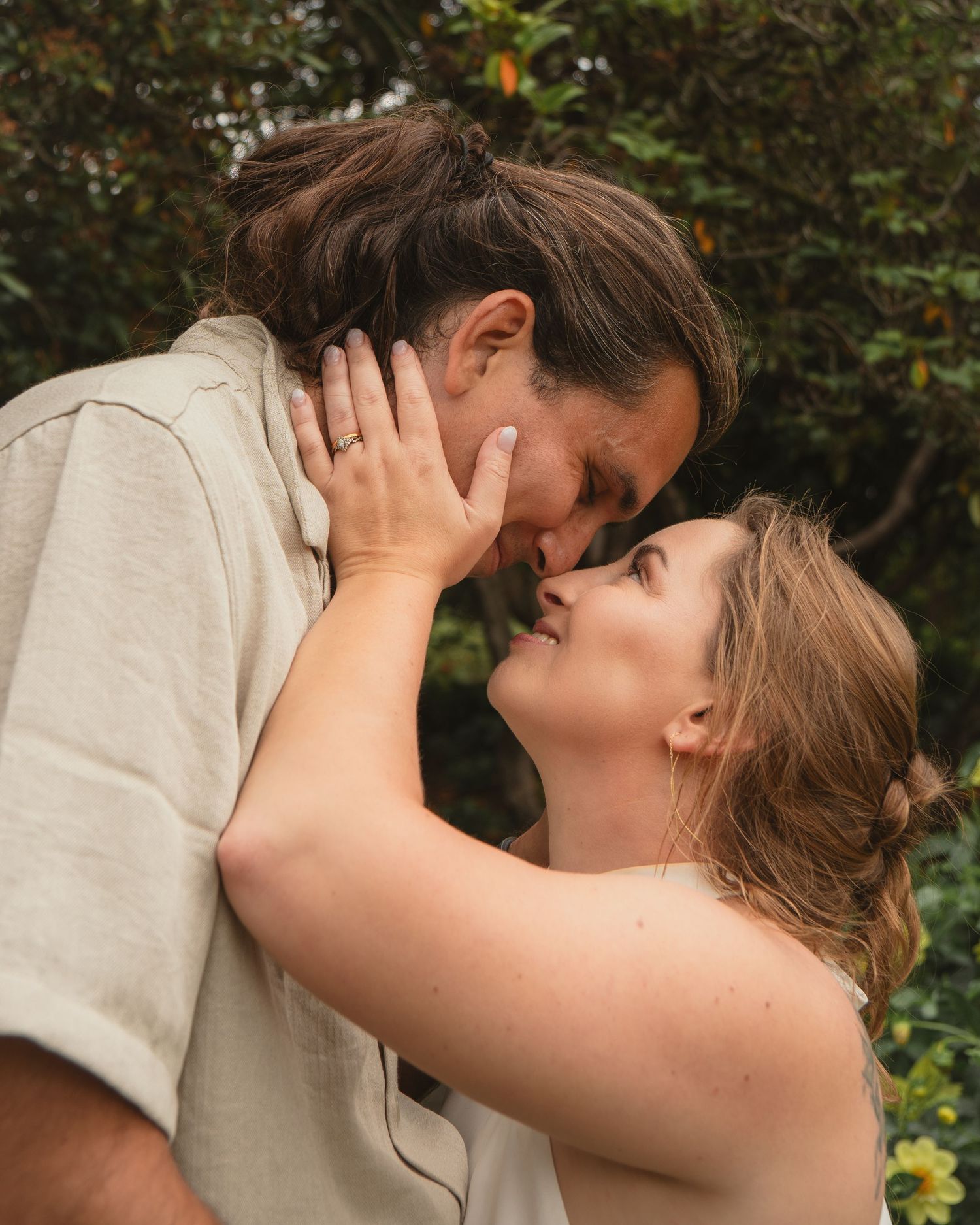 Close-up of a couple sharing a tender kiss outdoors with green foliage in the background.