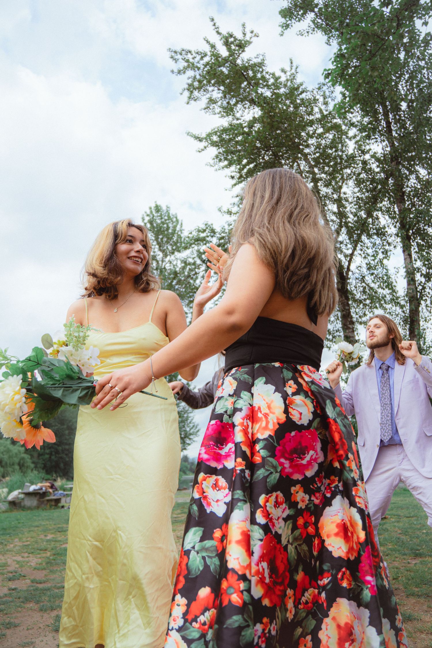 Wedding guests in colorful dresses celebrate bouquet toss at outdoor garden reception.