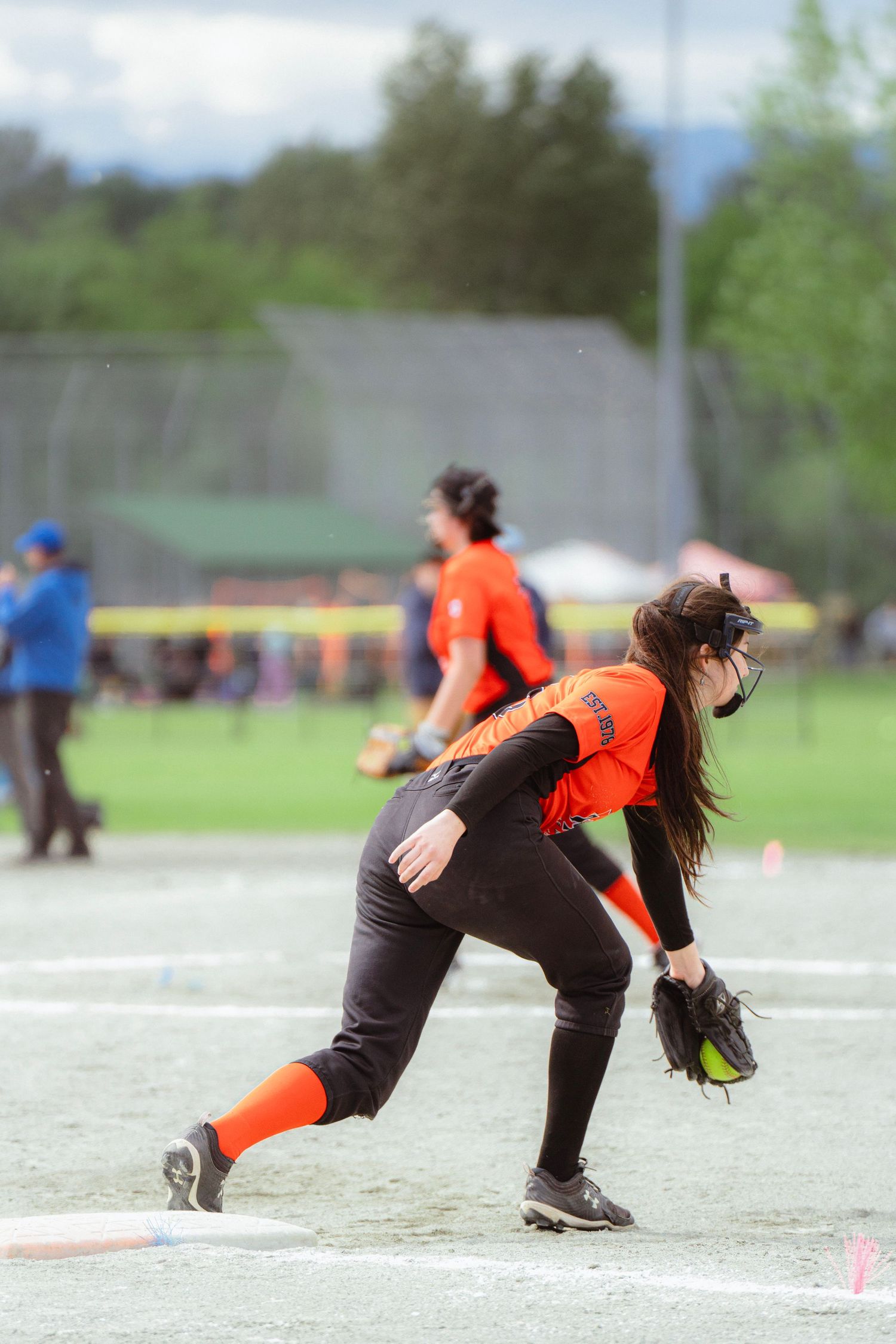 Female softball player in orange uniform fielding a ground ball at first base.