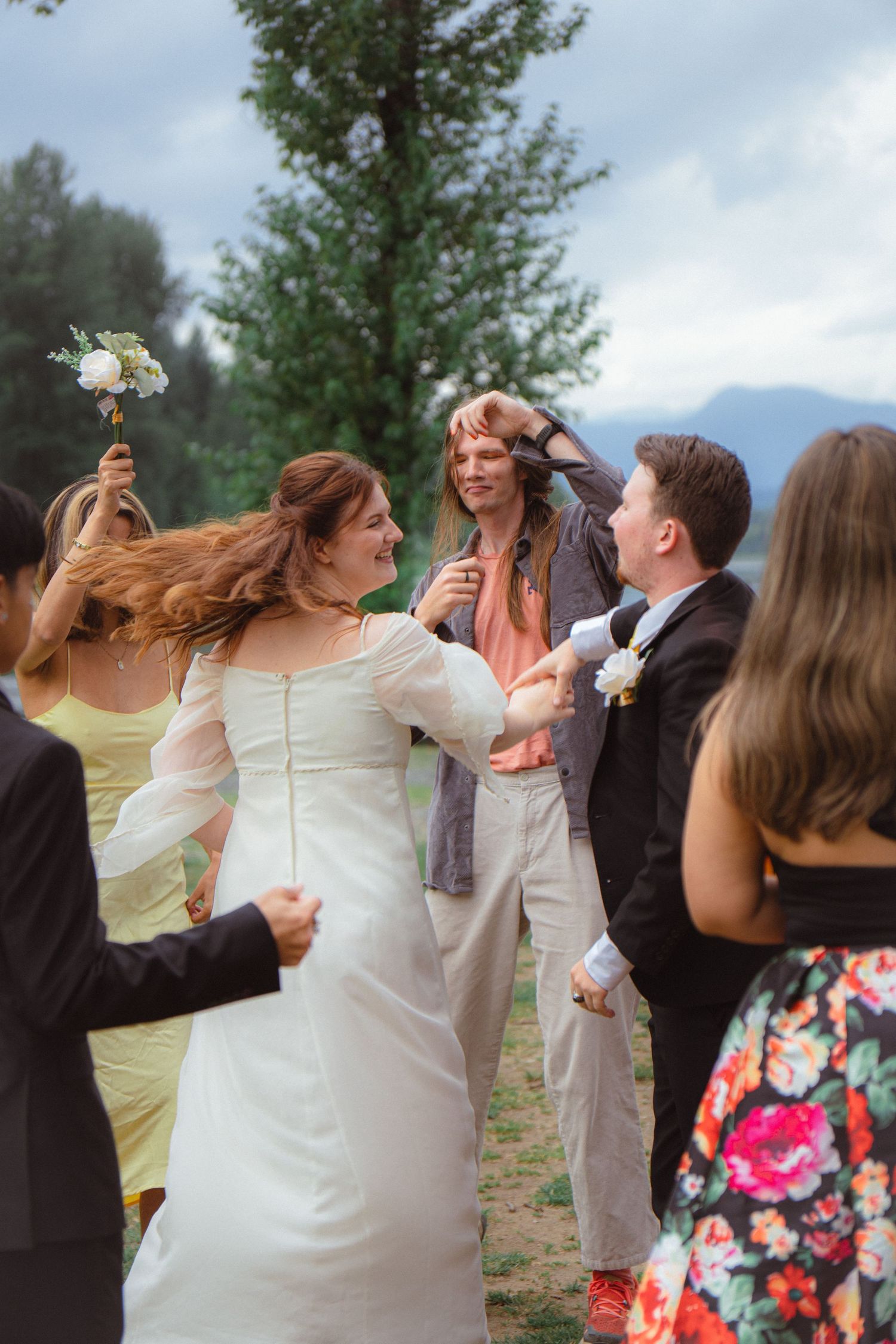 Bride and groom celebrating with guests in a lively outdoor wedding reception near mountains.