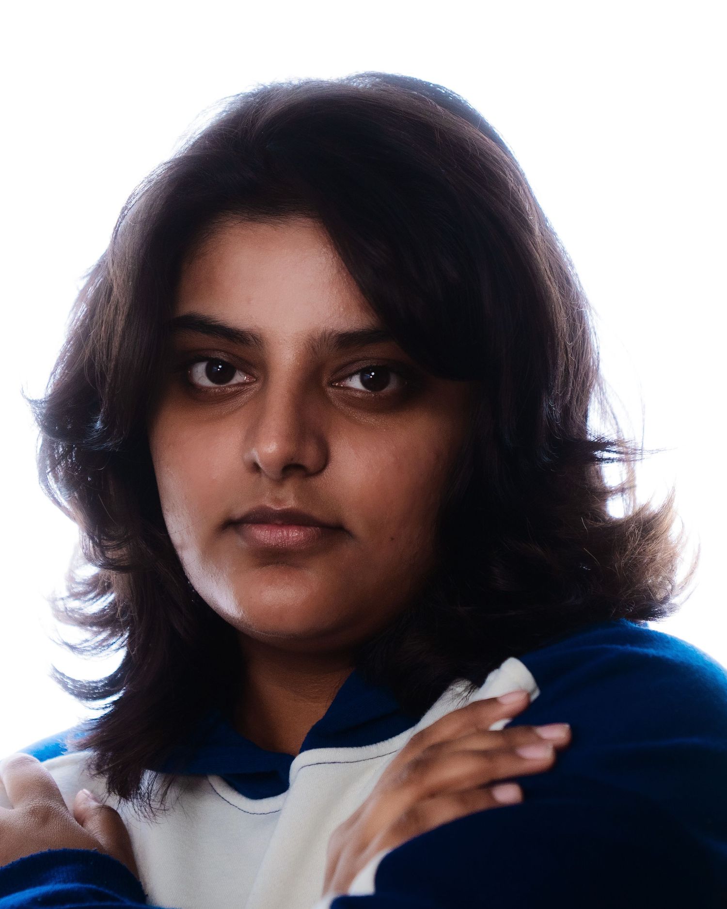Young woman with dark shoulder-length hair wearing a blue and white hoodie, dramatic portrait on white background.