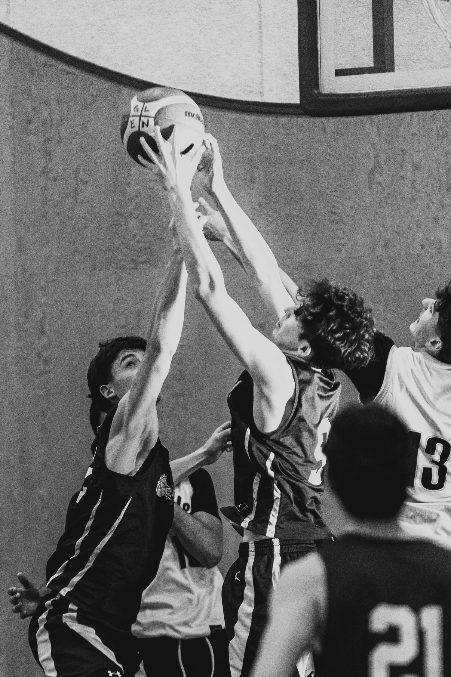 Black and white action shot of multiple basketball players jumping to contest the ball indoors.