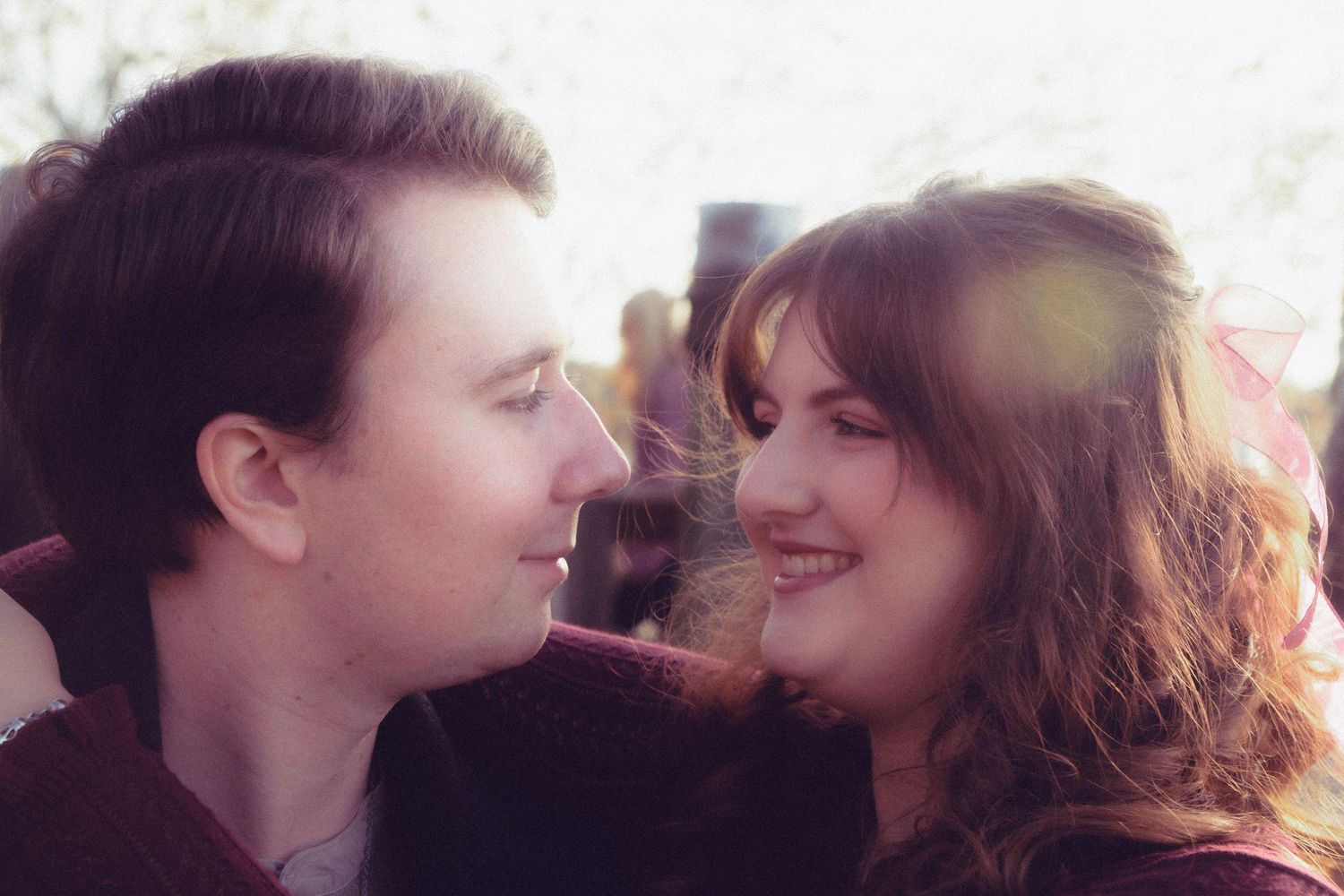 A romantic couple gazing at each other outdoors, bathed in soft sunlight with a warm, dreamy lens flare effect.