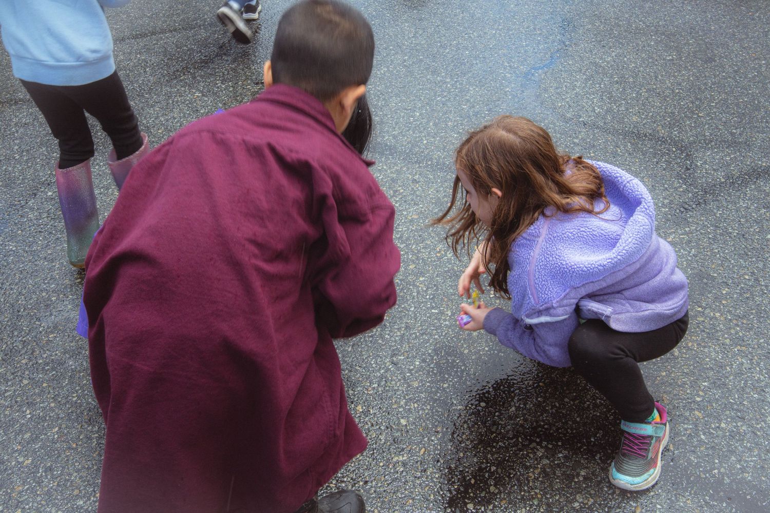 Two people crouching down examining something on wet pavement at outdoor festival.