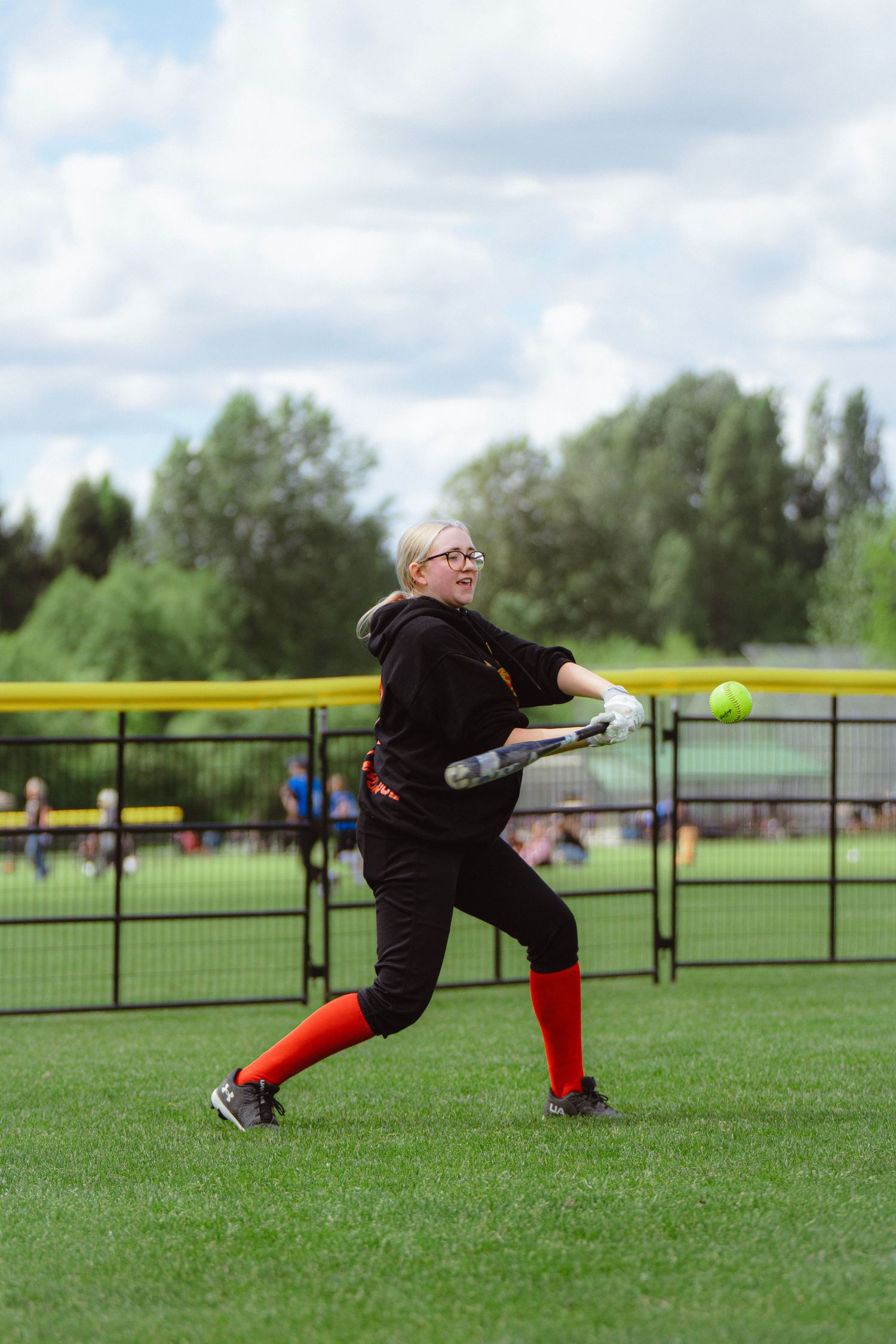 Blonde female softball player in glasses hitting softball during practice.