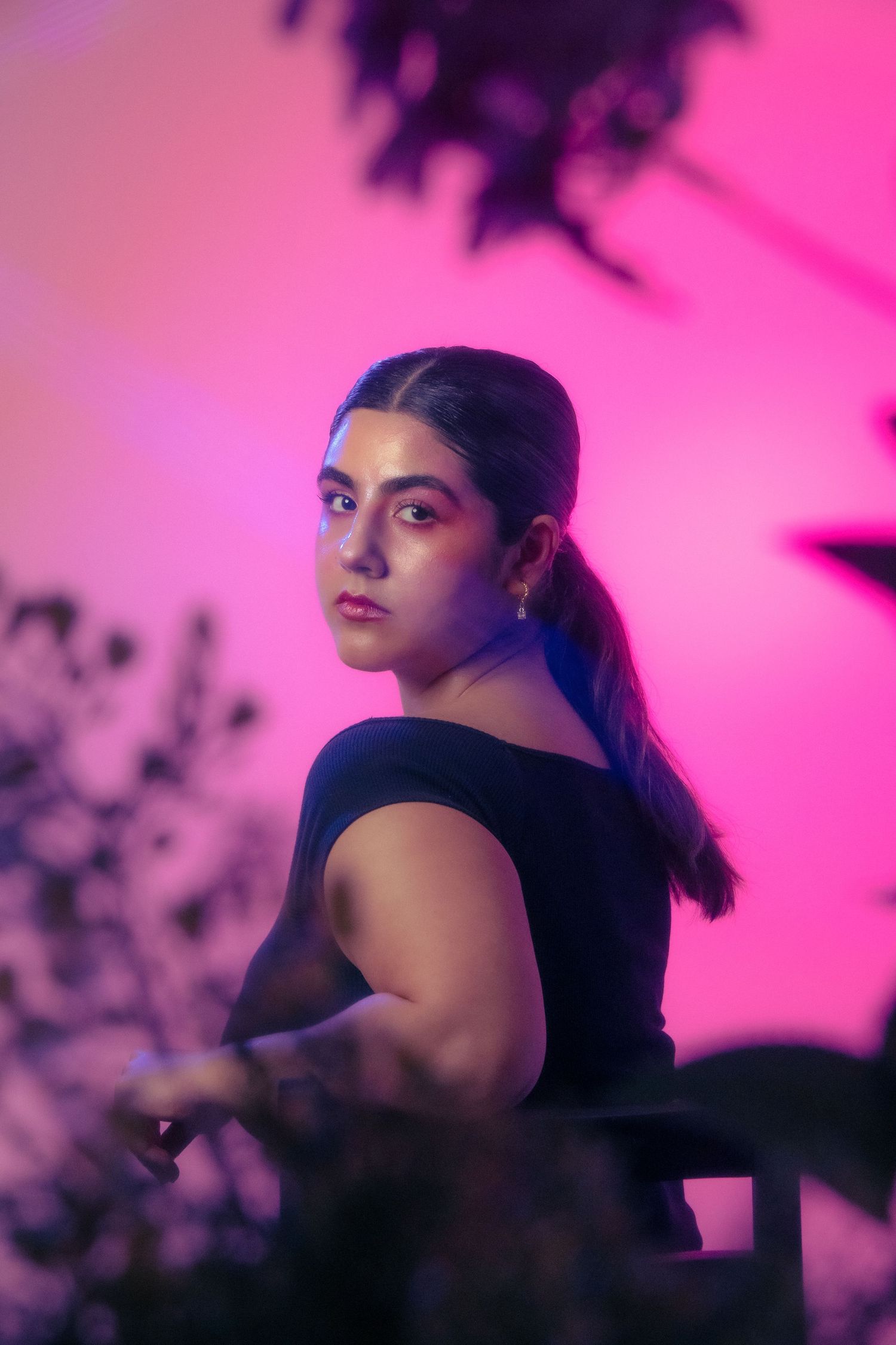 A young woman in a black top poses gracefully against a vivid pink background with plant silhouettes.