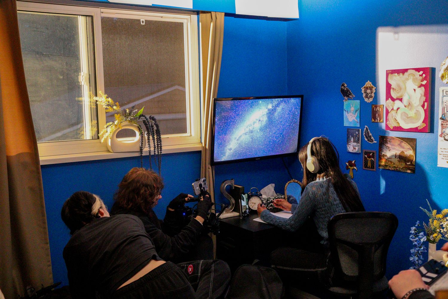 Film crew members work at a desk with monitors in a blue-walled production room.