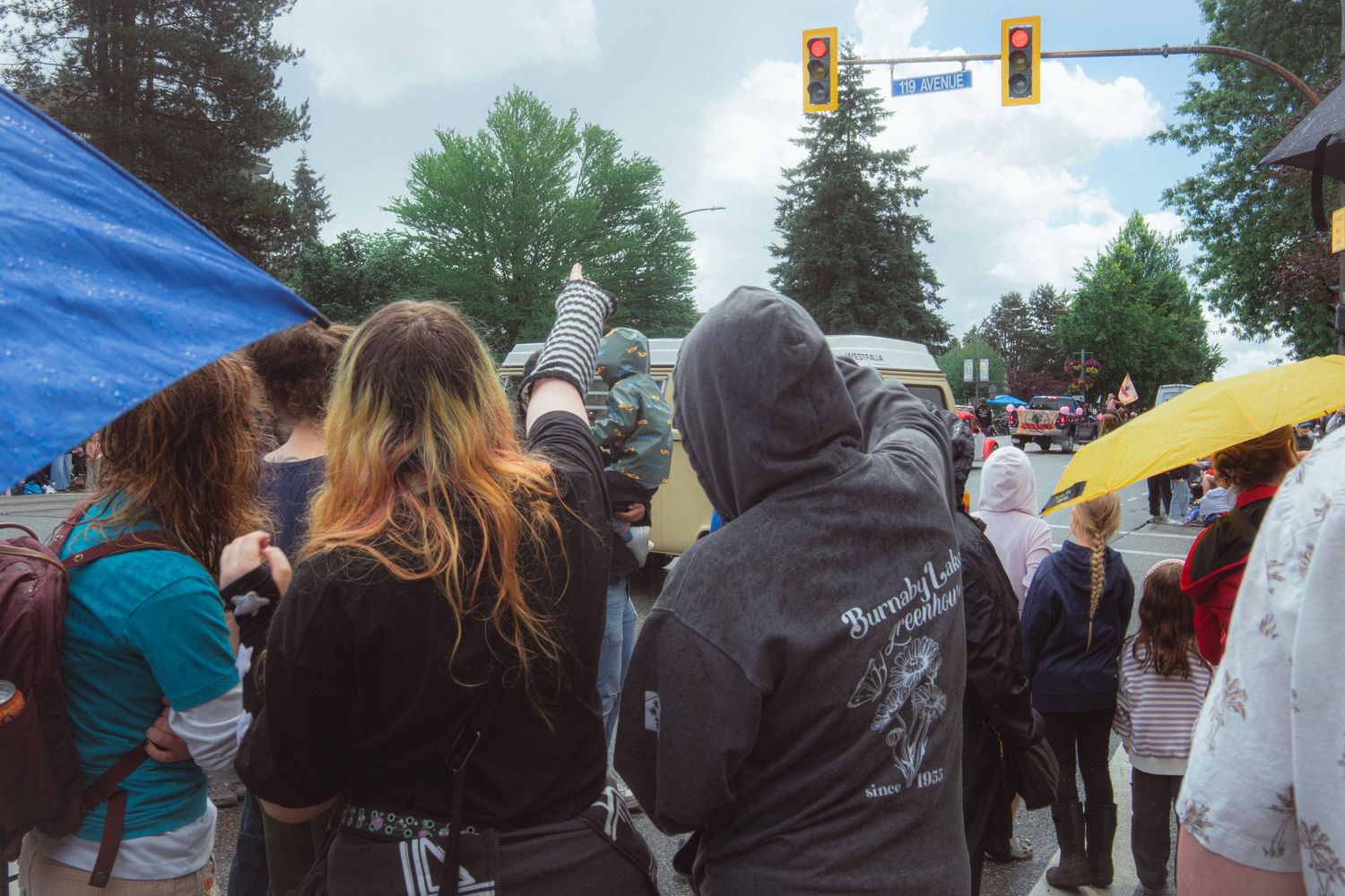 A crowd of parade spectators stands on a street corner under traffic lights on a cloudy day.