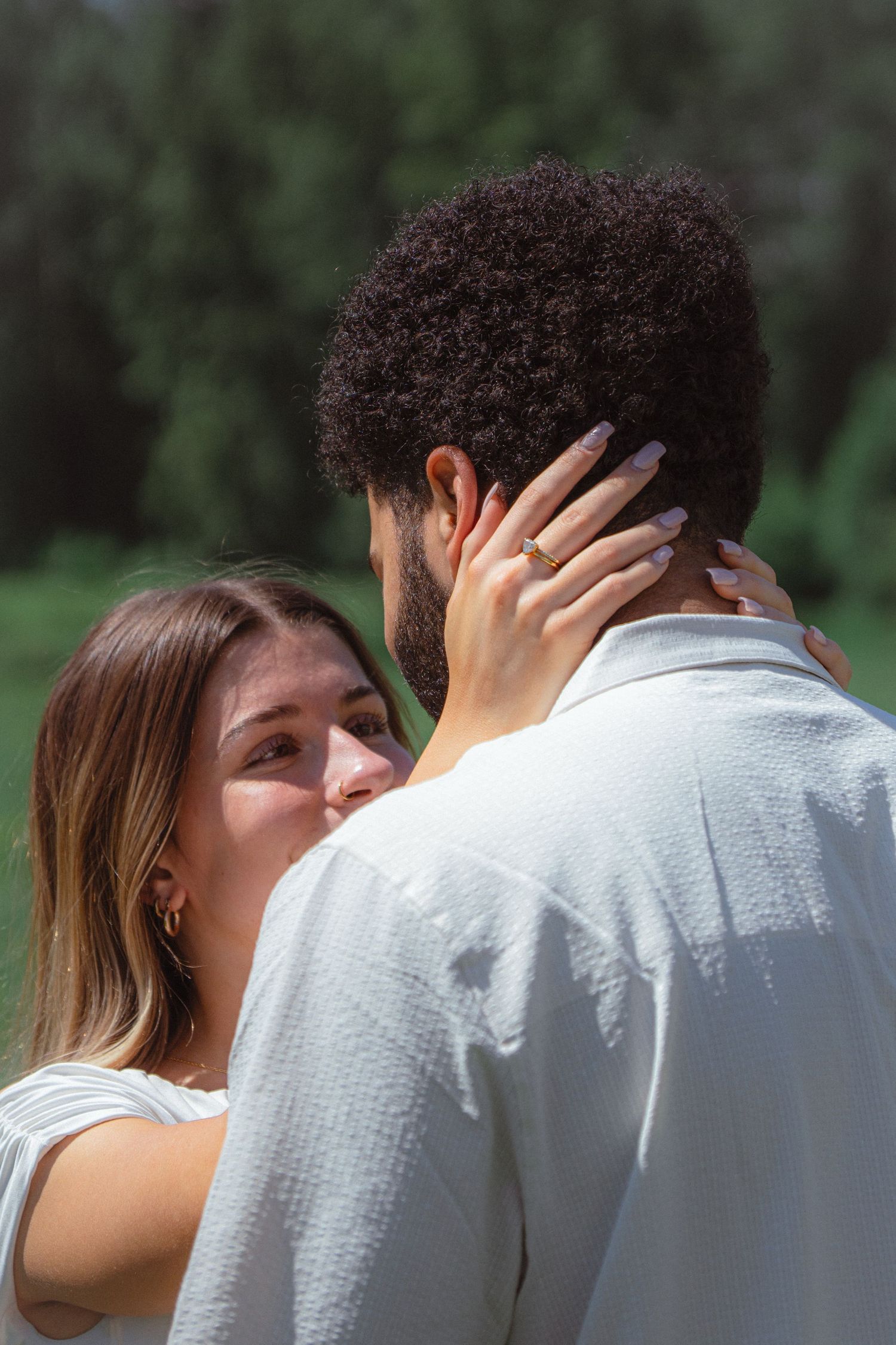 A woman tenderly holds a mans face as they share an intimate moment outdoors in soft sunlight.