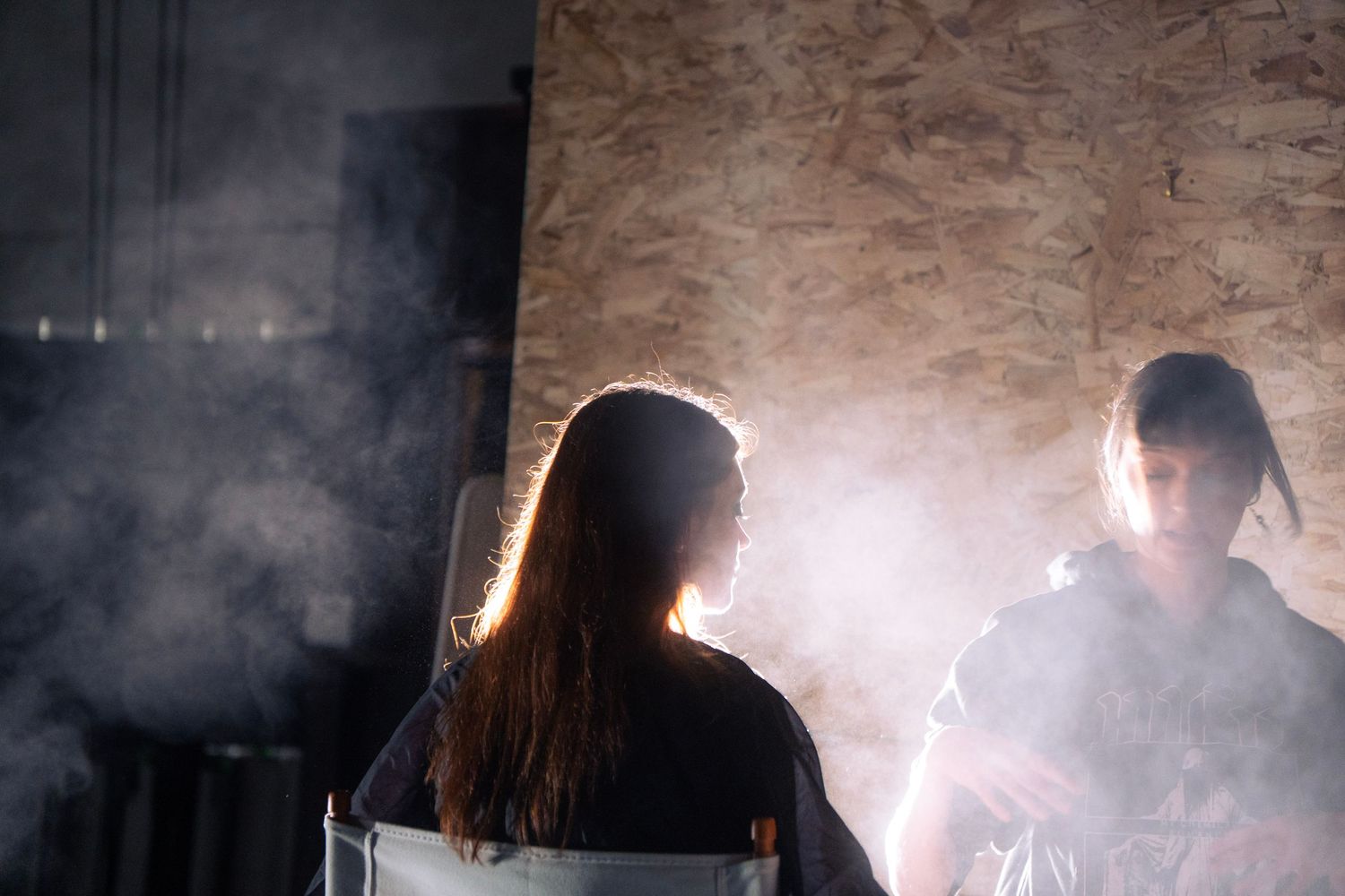 Two people sitting in a smoky dark studio with dramatic backlighting during a film production.