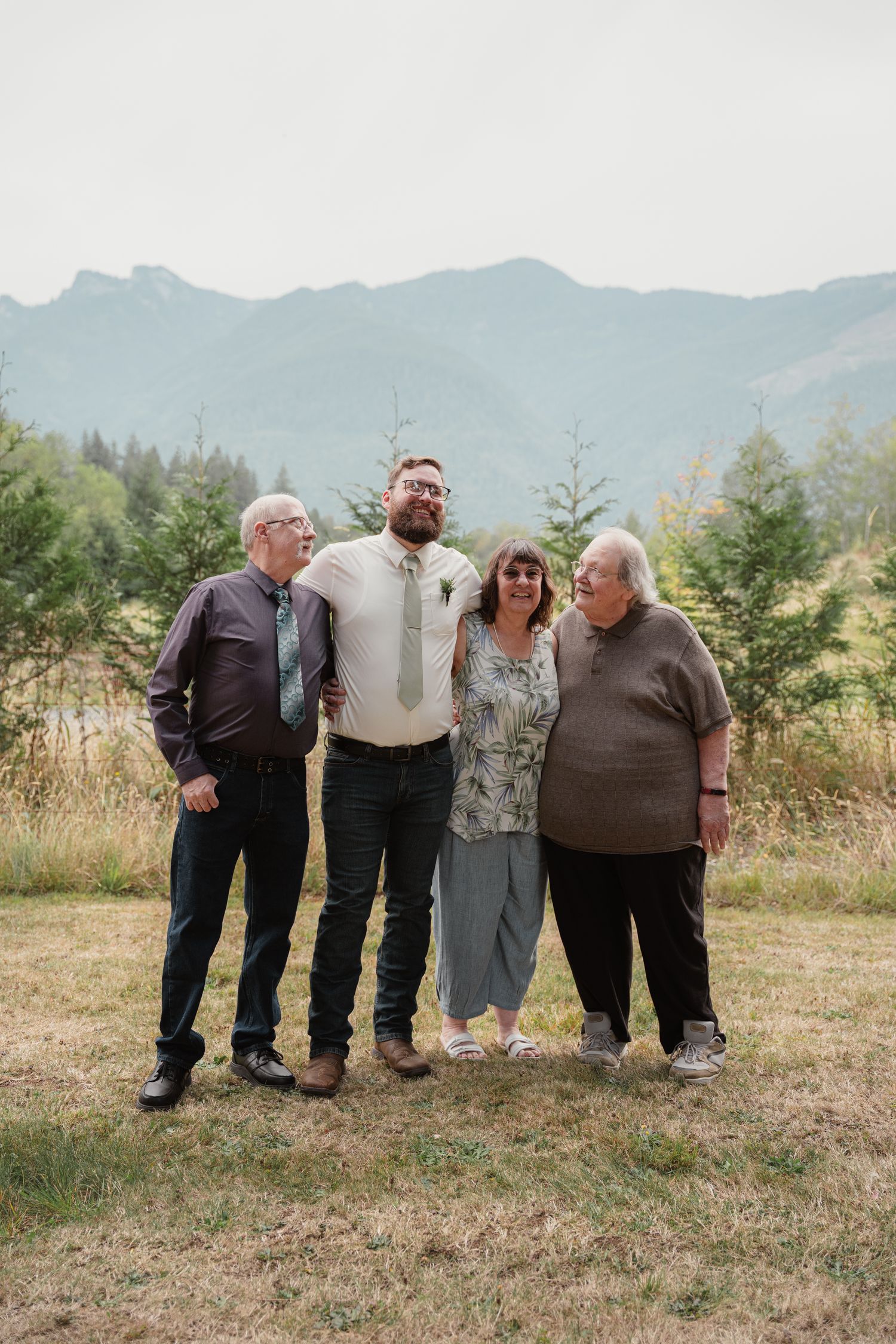 Groom with green tie poses with three family members against a scenic mountain backdrop at wedding.