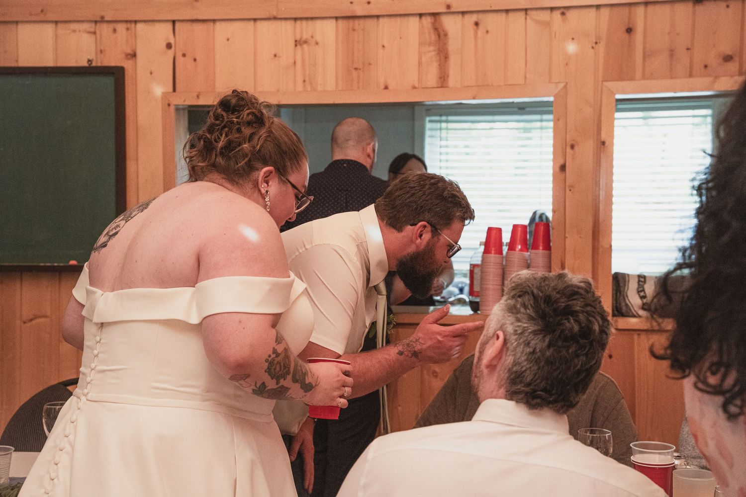 Bride and groom share an intimate moment with guests at a rustic wooden wedding reception venue.