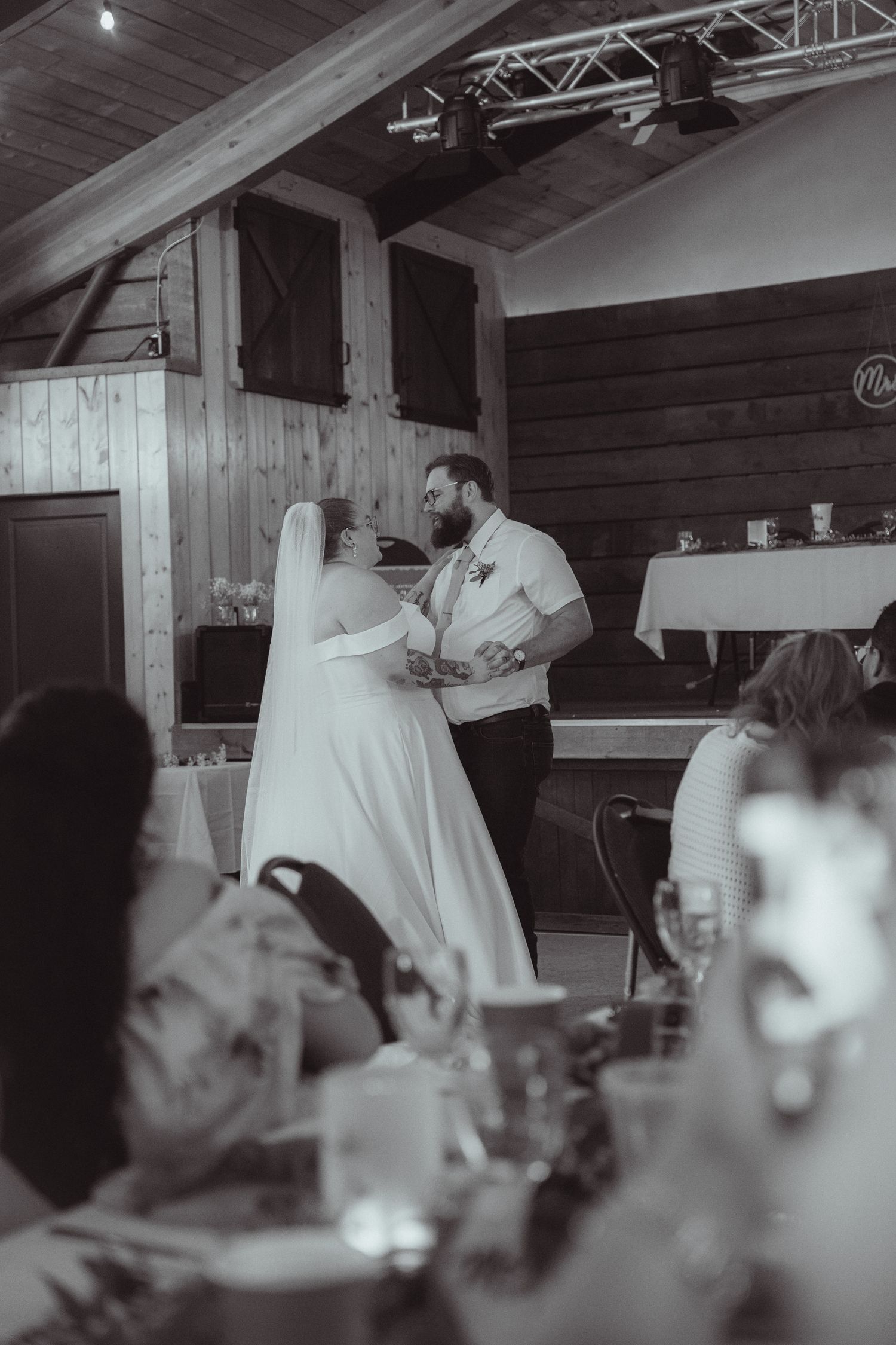 Bride and groom share their first dance in a rustic barn wedding venue, captured in black and white.