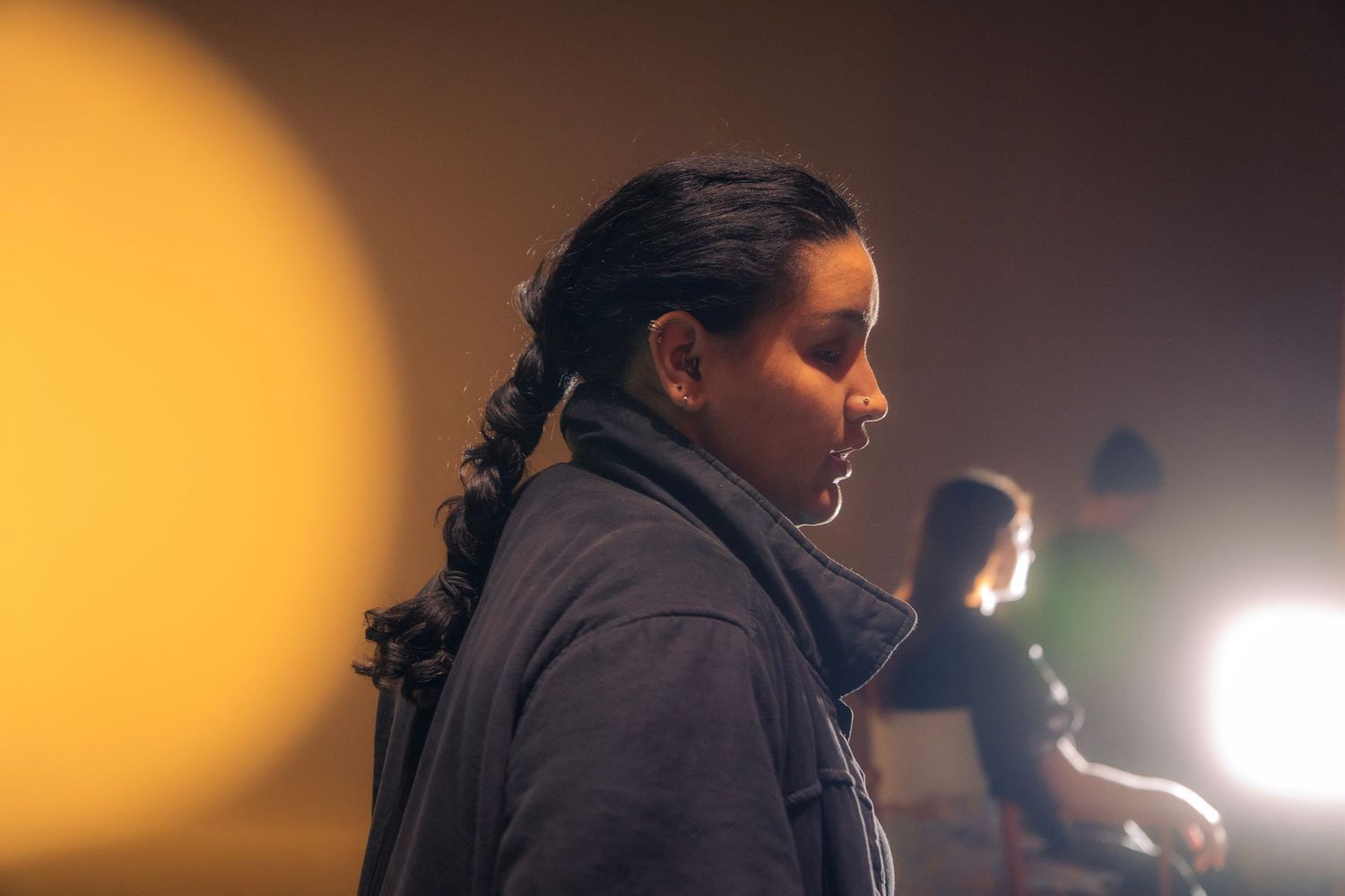 Woman with braided hair in profile view with warm yellow bokeh light in a dark film studio.