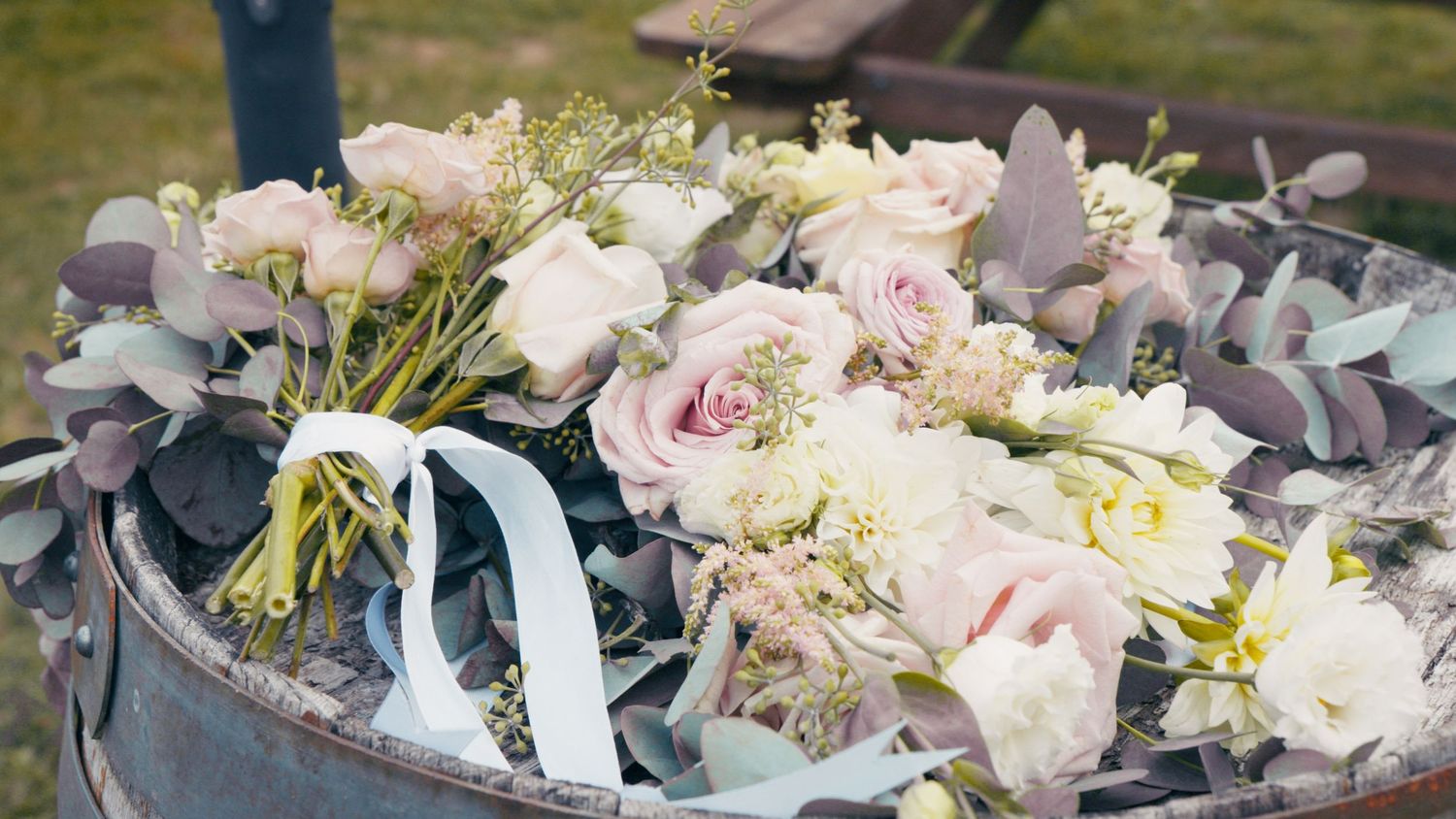 Elegant bridal bouquet of blush pink roses and white flowers with eucalyptus greenery resting in a vintage metal bucket.