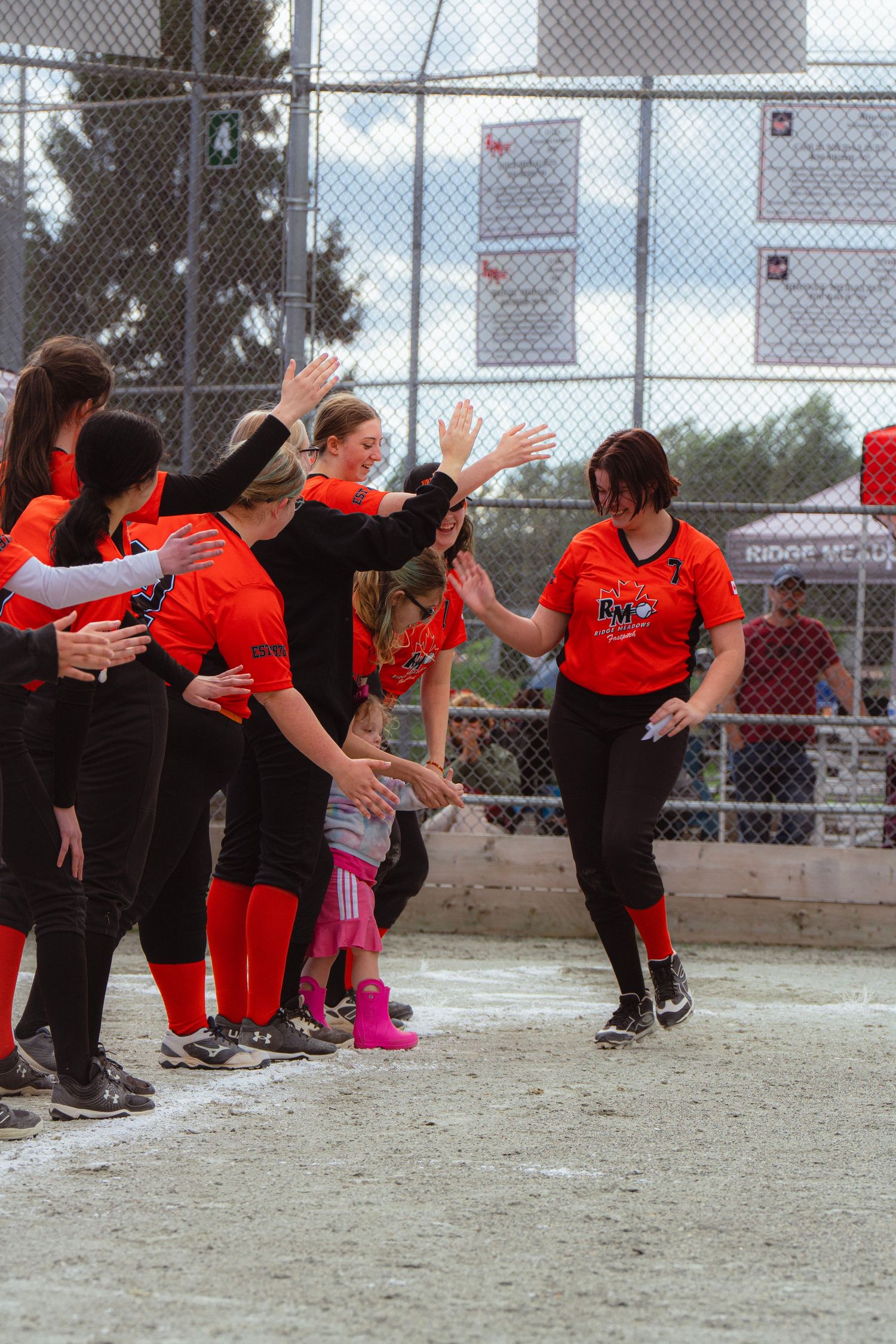 Female softball team in red and black uniforms high-fiving player returning to dugout after scoring.