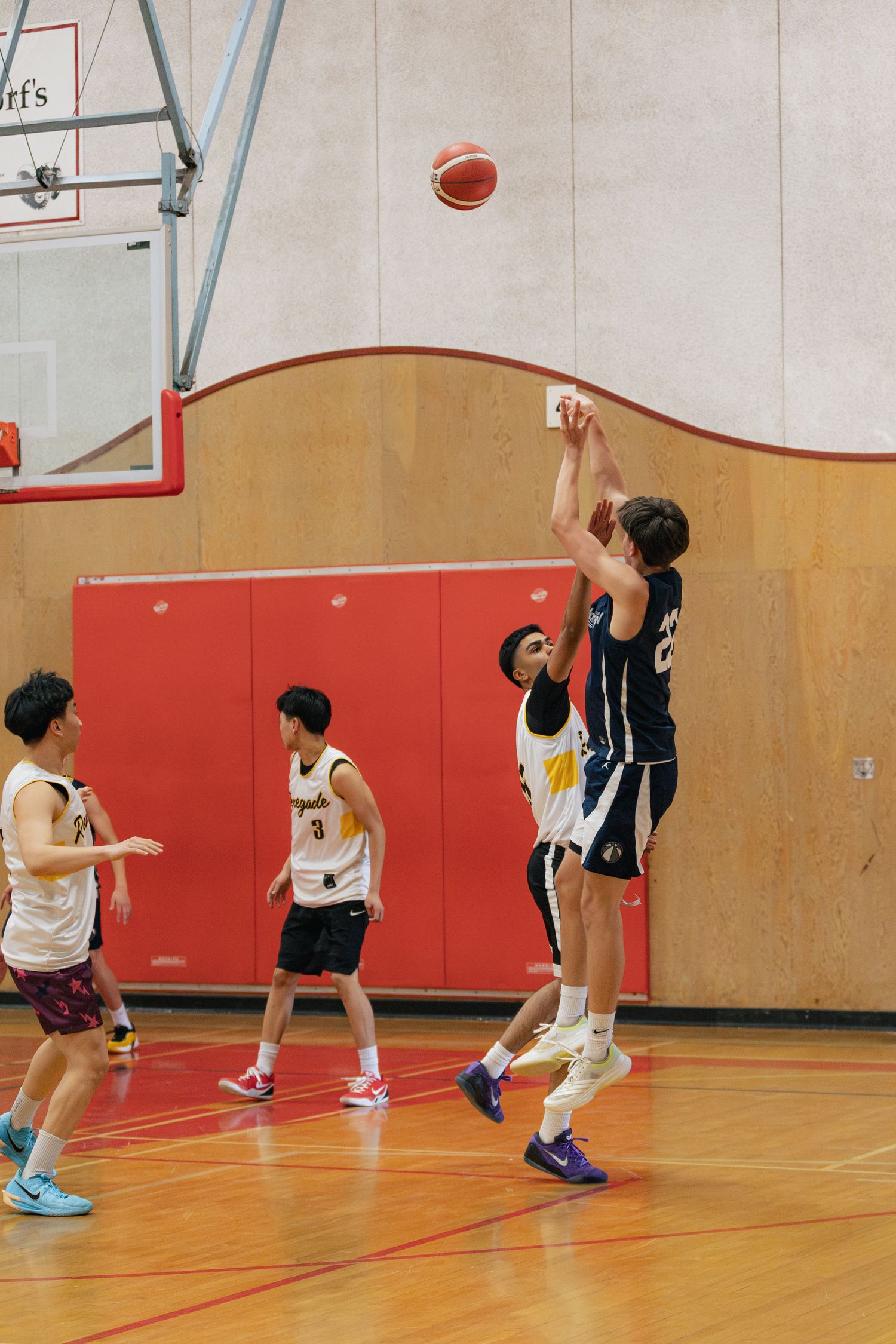 Basketball player #22 releases a jump shot over a defender during a competitive indoor youth basketball game.