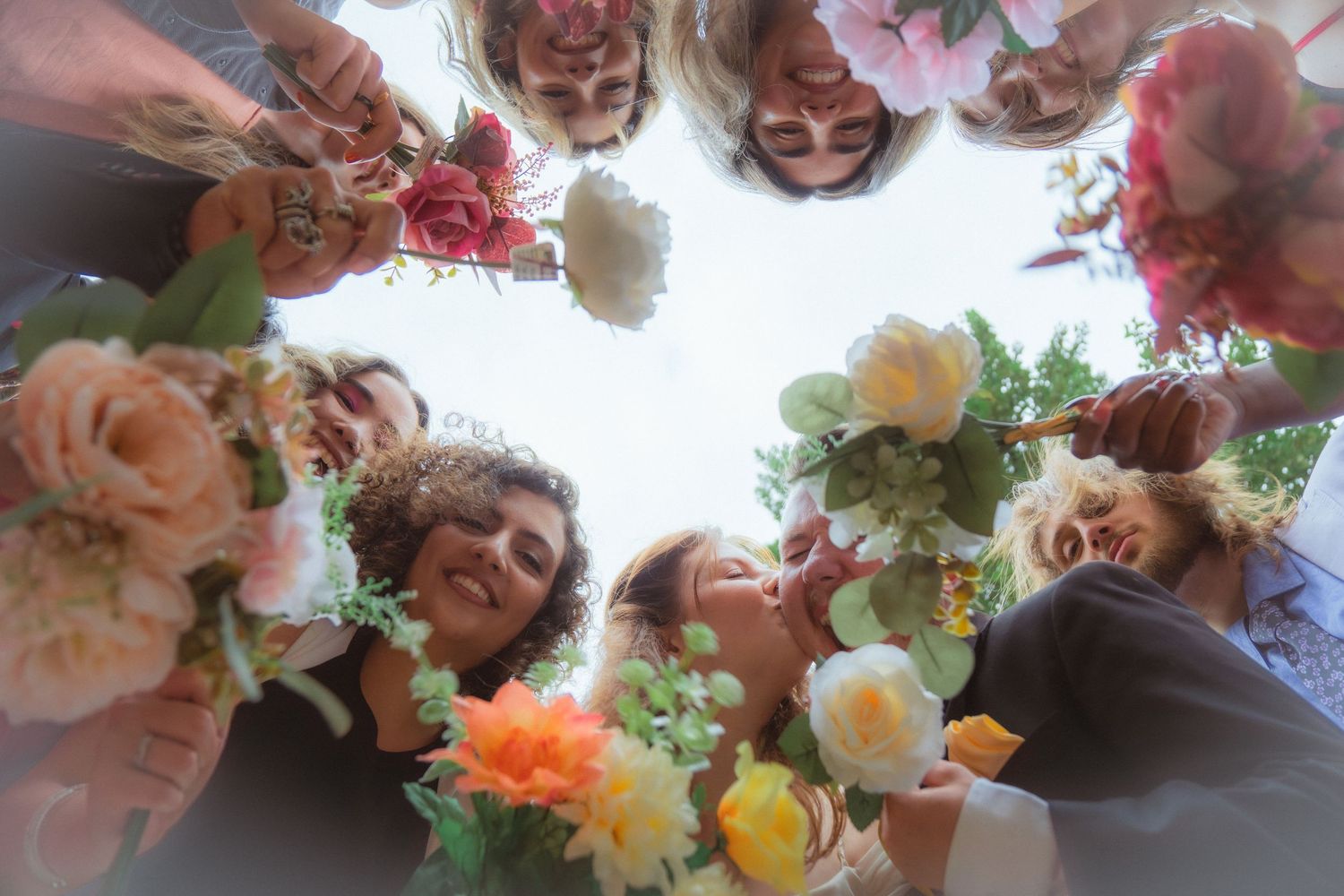 Low angle view of smiling wedding guests forming circle holding colorful floral bouquets.