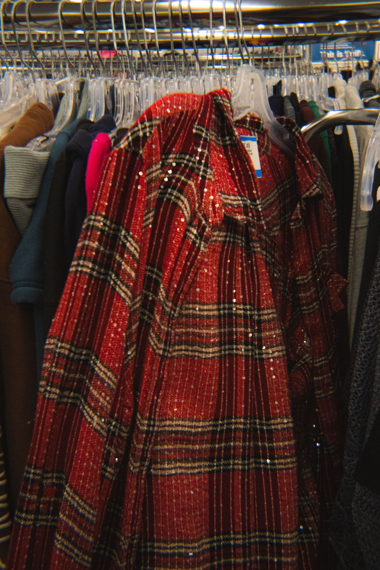 Red plaid sequined skirt hanging on a rack among other clothes at a thrift store.